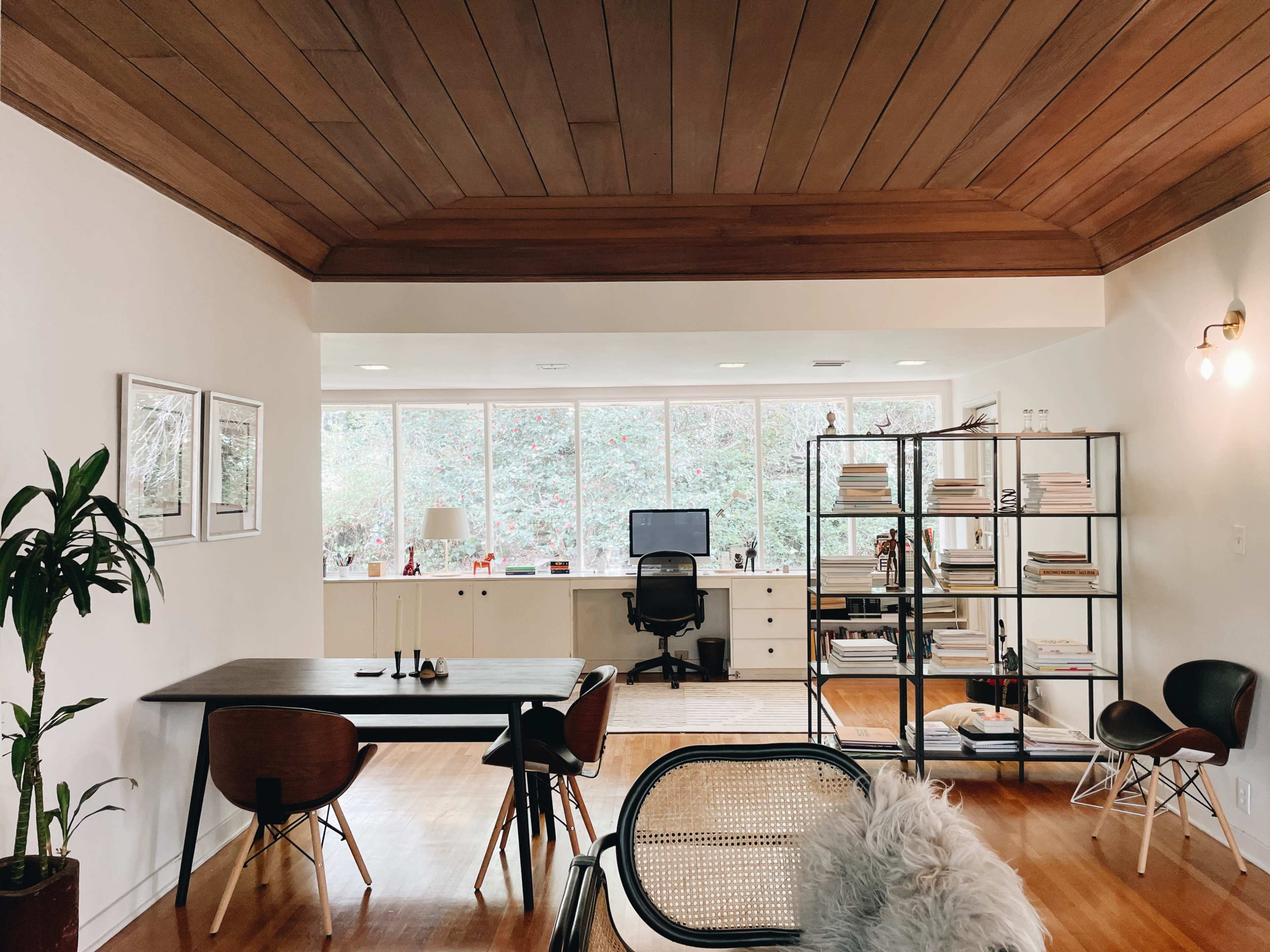 A modern home office with a large window, a desk and chair, and a bookshelf filled with neatly arranged books.