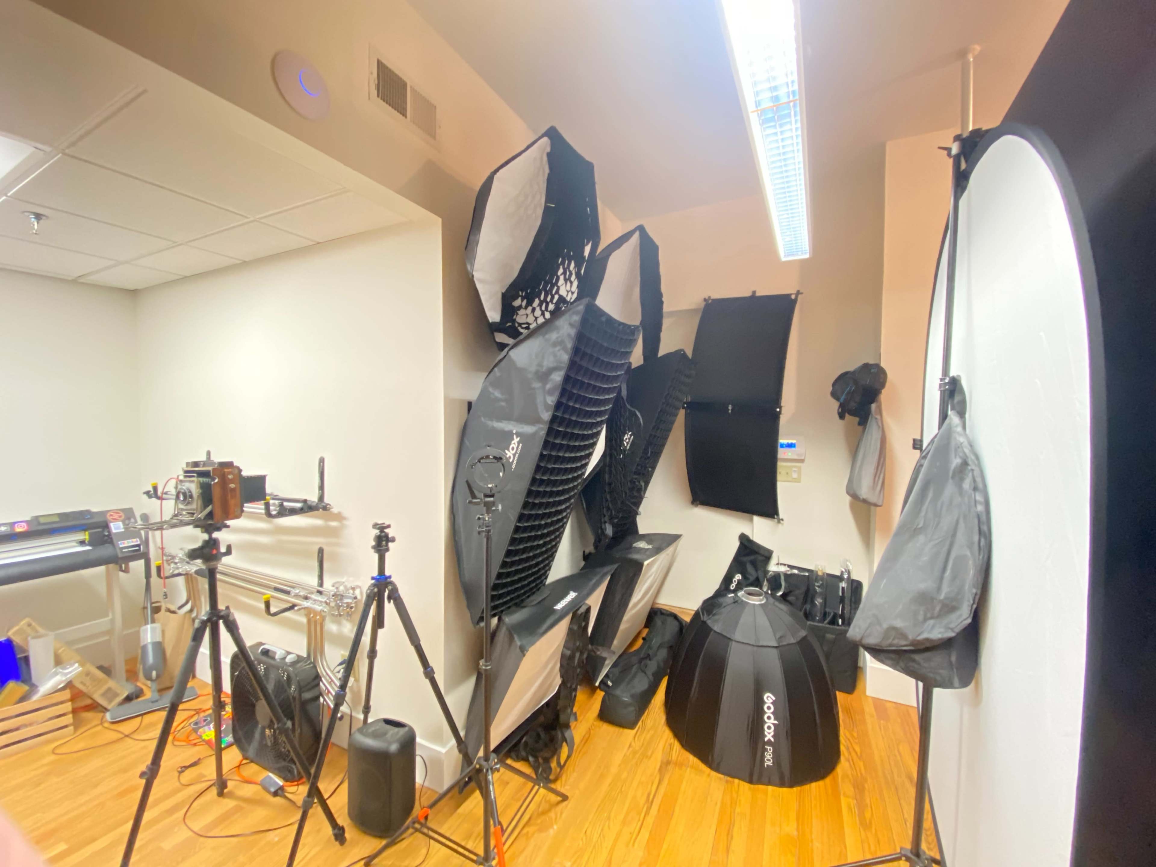 A photography studio is filled with various lighting equipment, backdrops, and stands arranged along the walls.