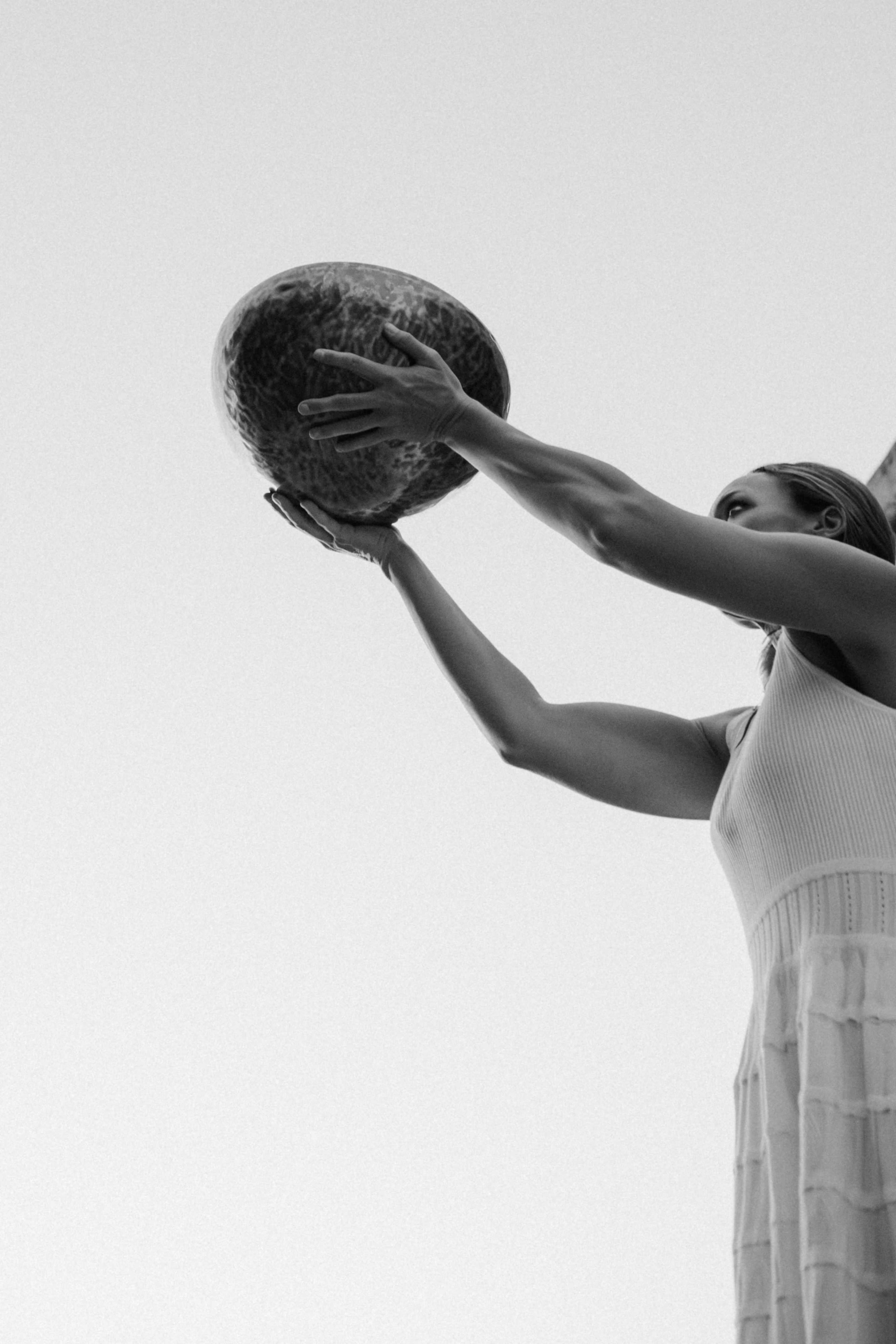 A person holds a large bowl above their head against a clear sky.