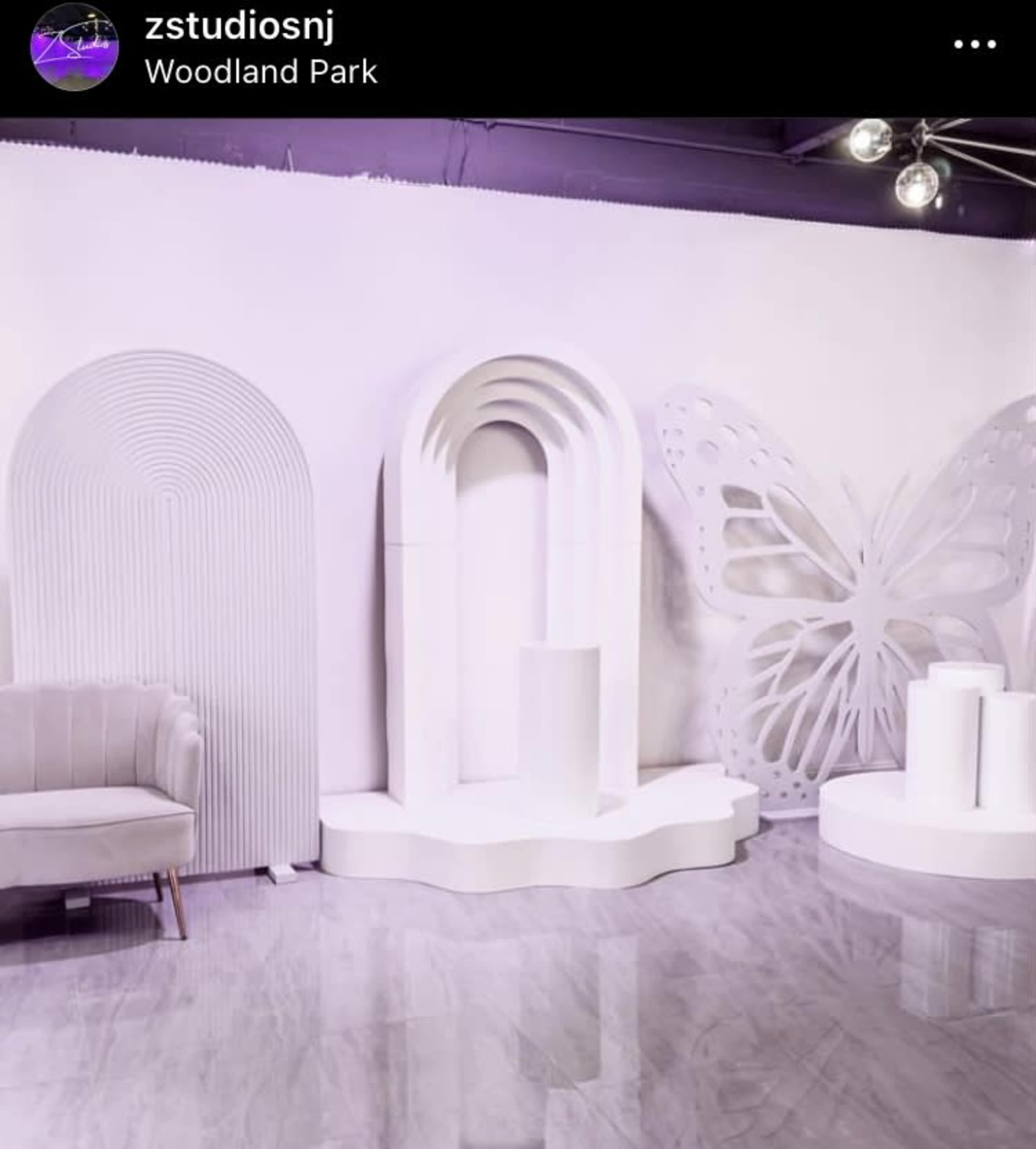 The image shows a modern studio interior featuring white decorative elements, including arches and a large butterfly design on the wall.