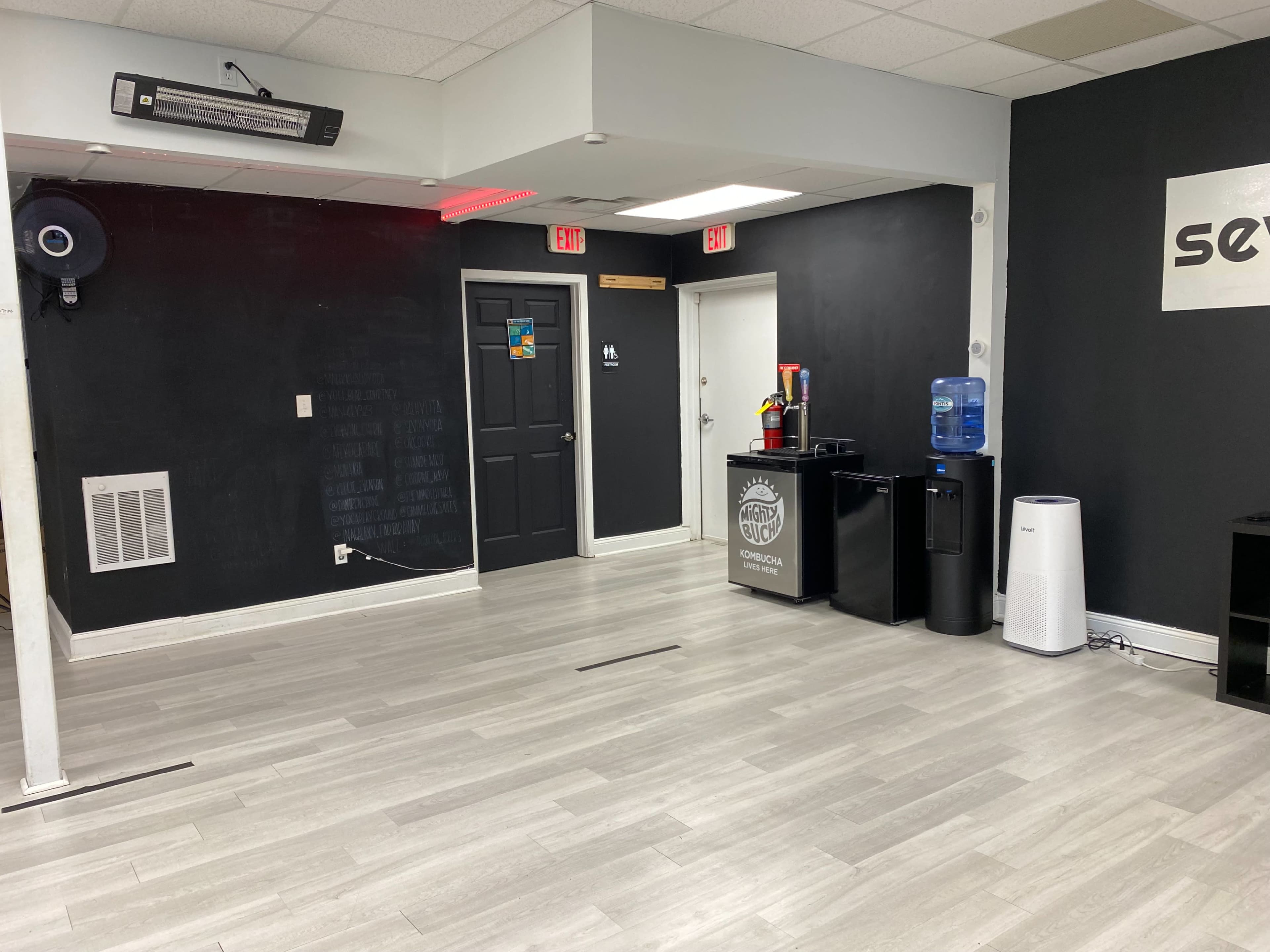 A modern, sparsely furnished room with gray flooring, a water cooler, and a black wall with white signage.