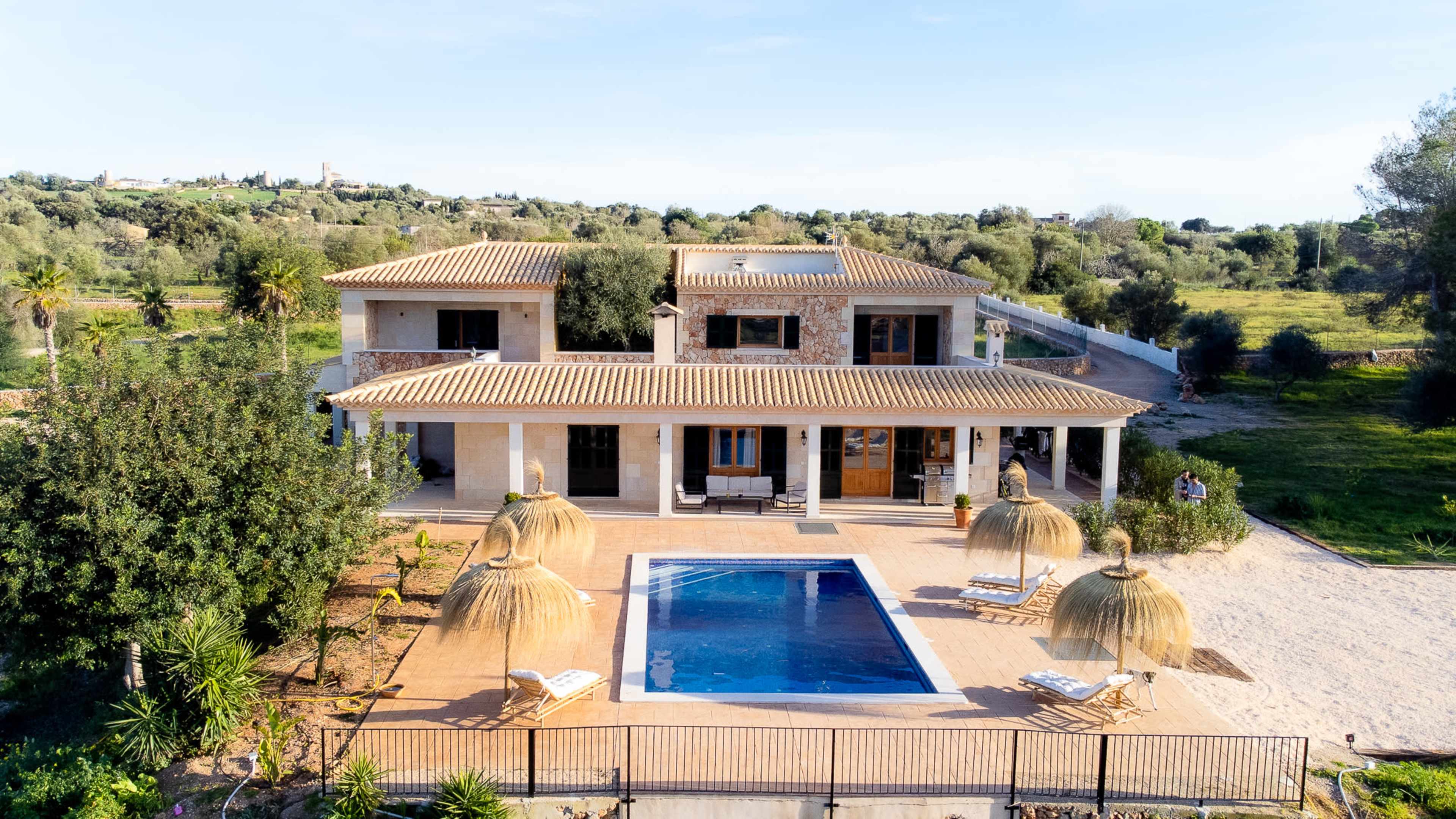 A large, two-story house with a swimming pool is surrounded by greenery and outdoor seating areas.