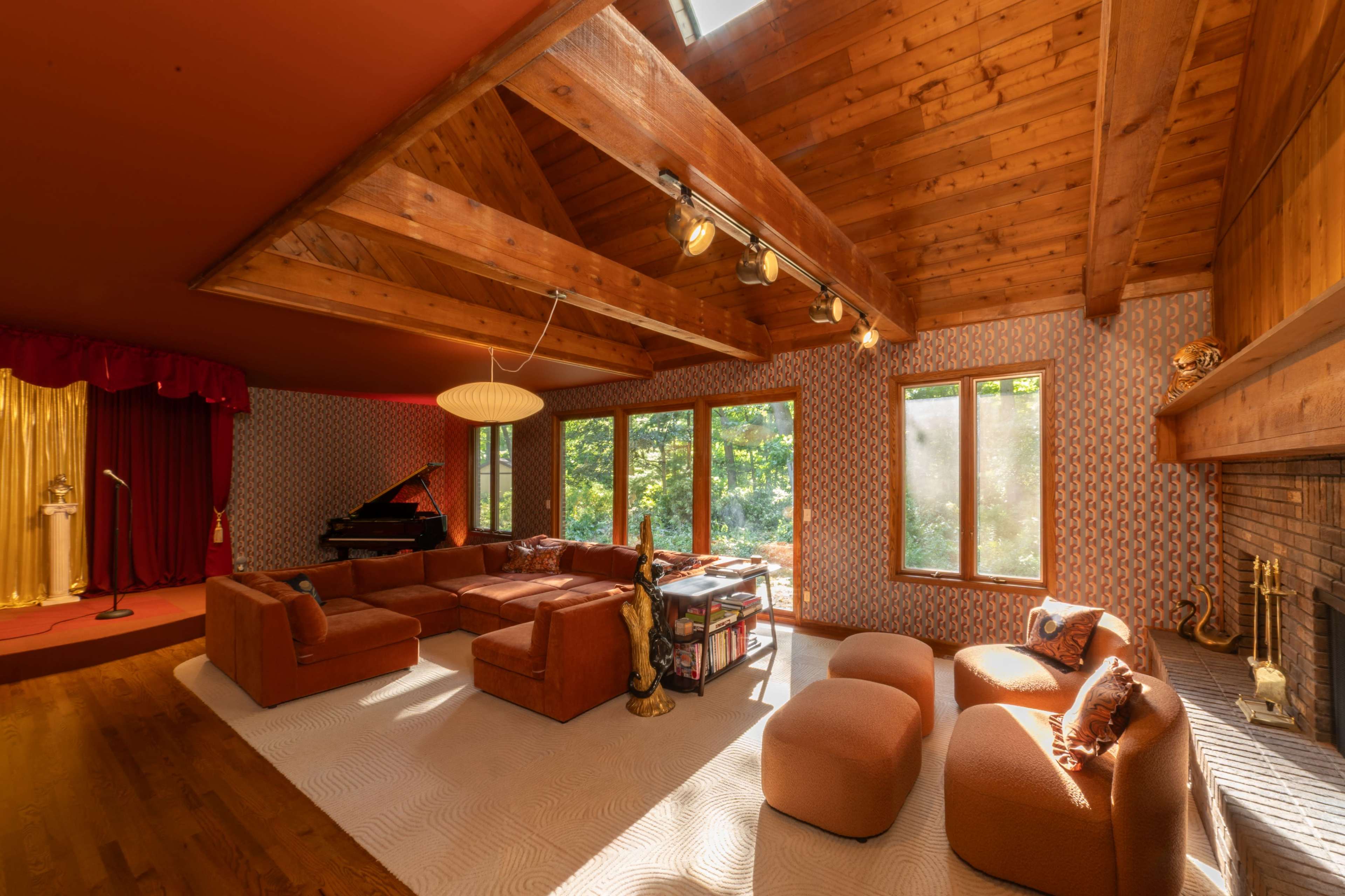 The image shows a spacious living room with a vaulted wooden ceiling, large windows, and a mix of comfortable seating arrangements.