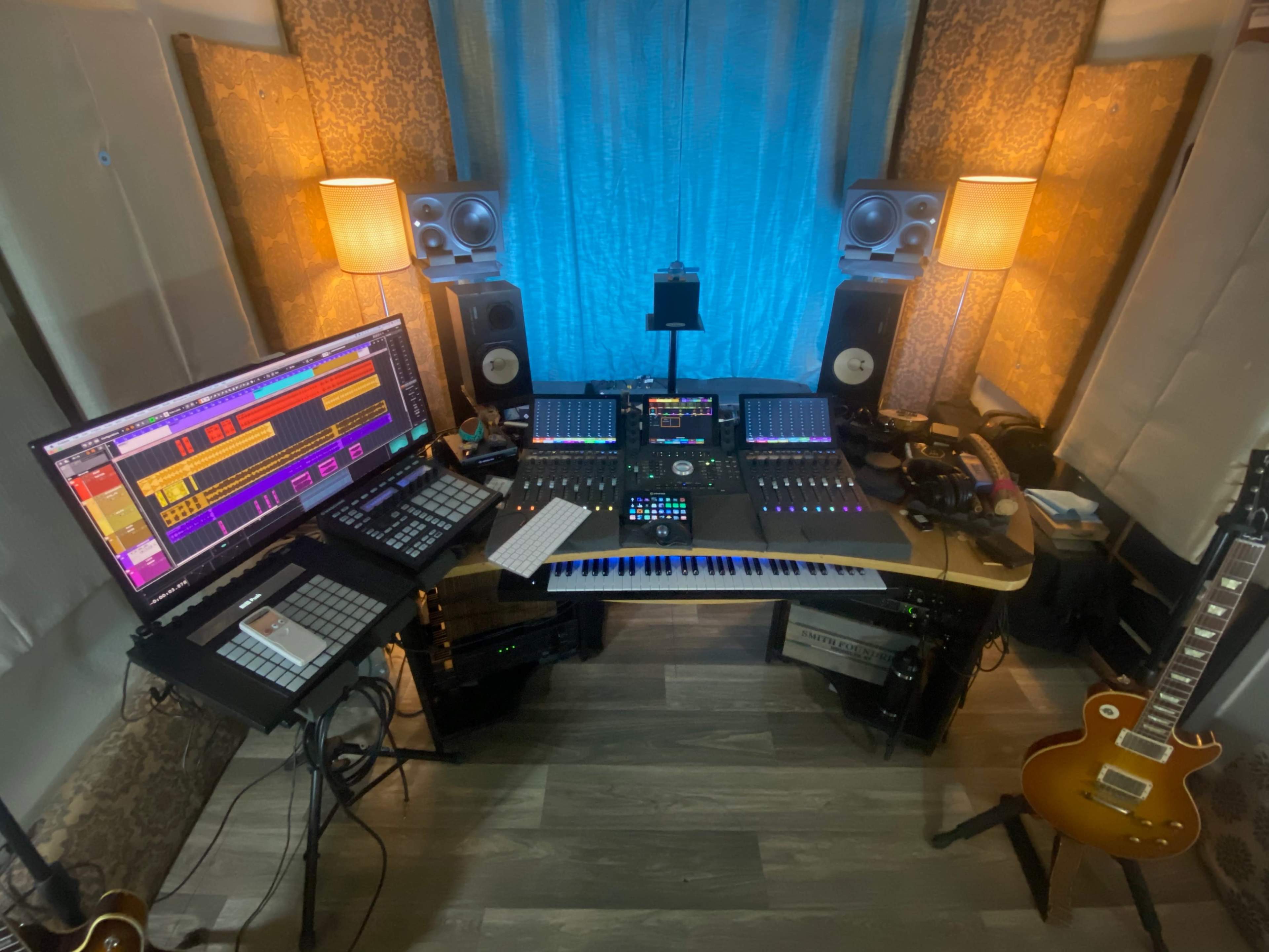 A sound recording studio with a keyboard, computer monitors, and various audio equipment arranged around a central workstation.