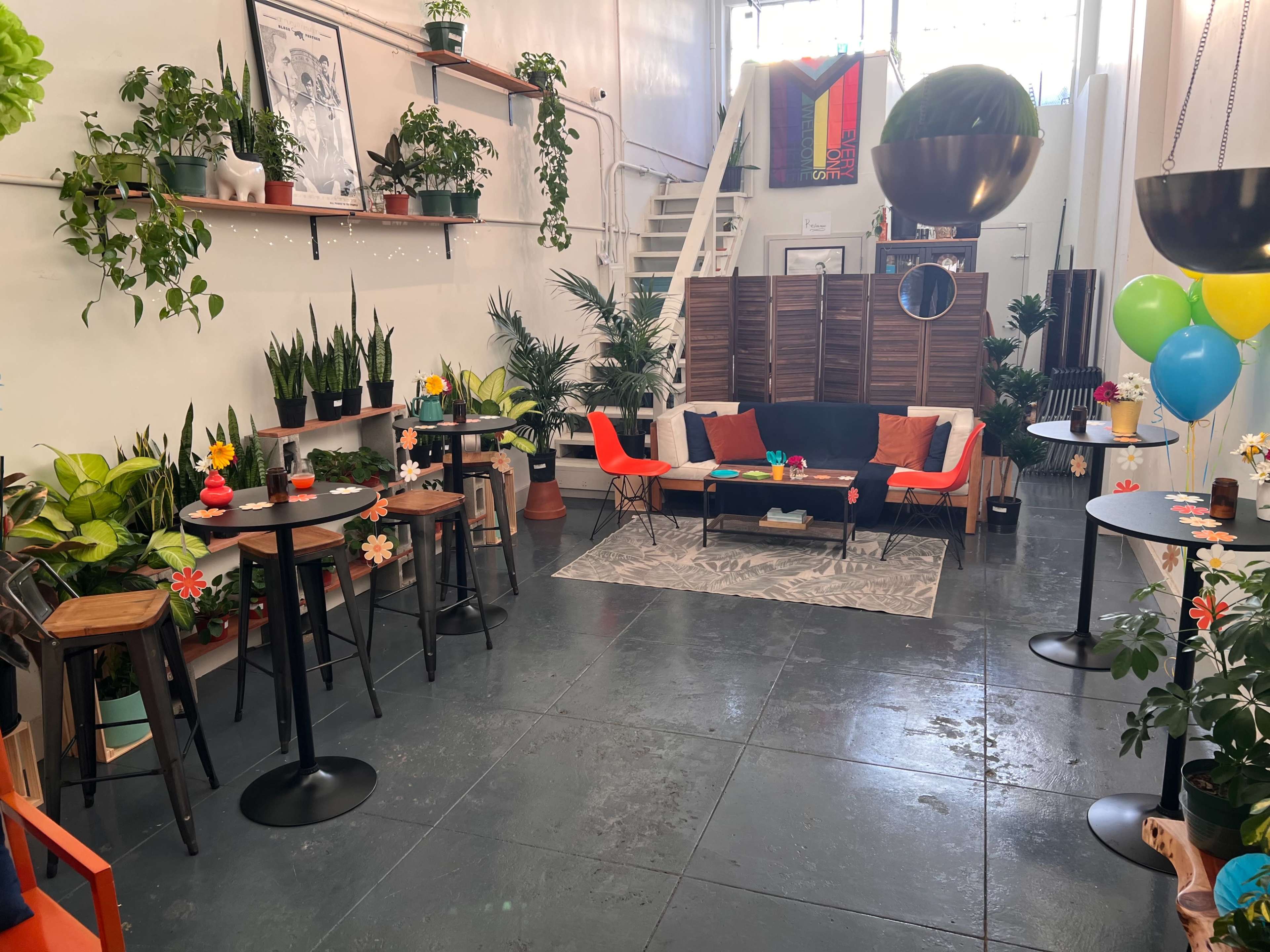 A brightly decorated indoor space with seating areas, plants, and colorful balloons arranged for a gathering or event.