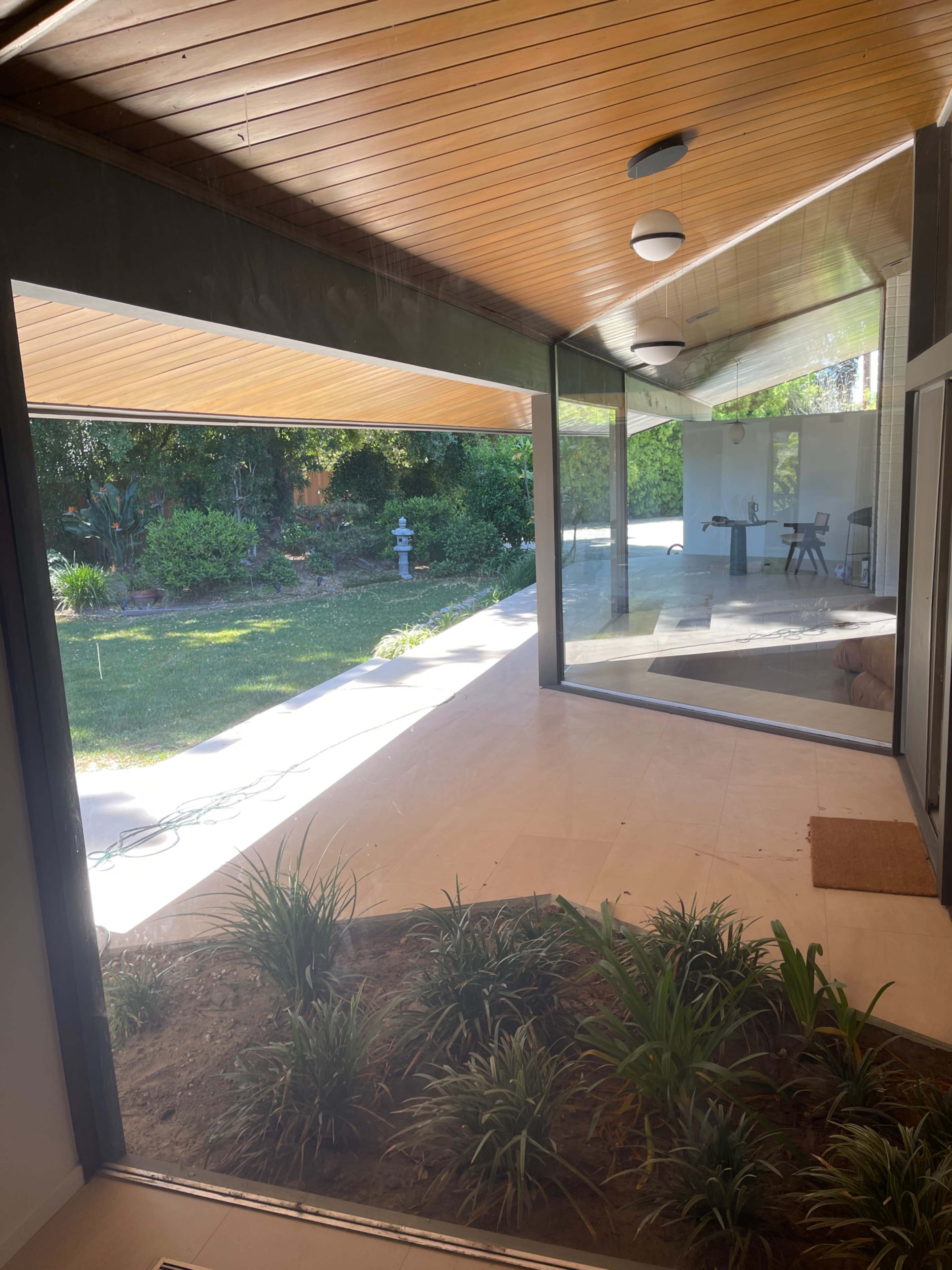 A room with large glass walls overlooking a landscaped garden, with a wooden ceiling and tile flooring.