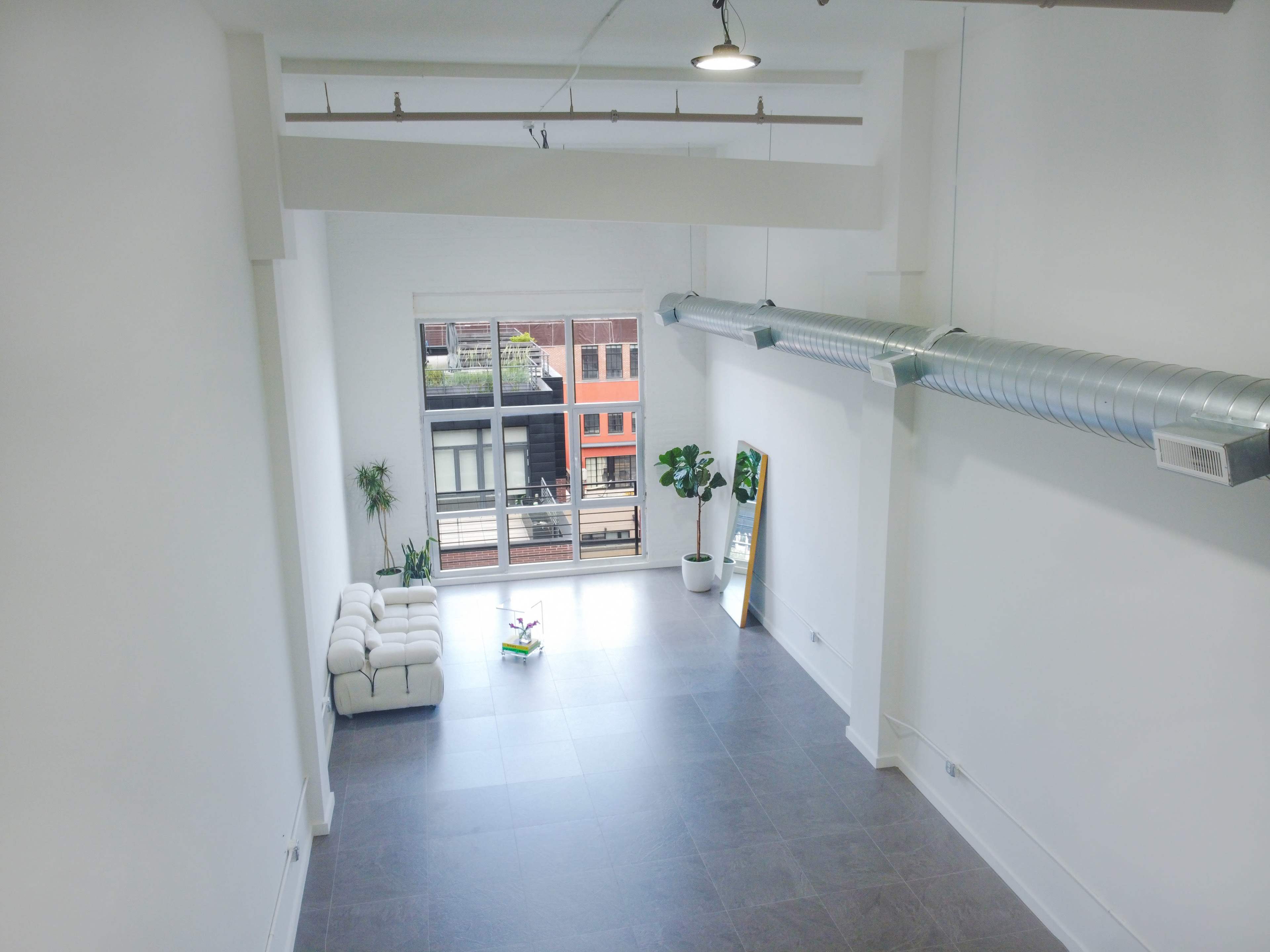 A spacious, minimalist room with large windows overlooking an outdoor area and featuring a sofa and potted plants.