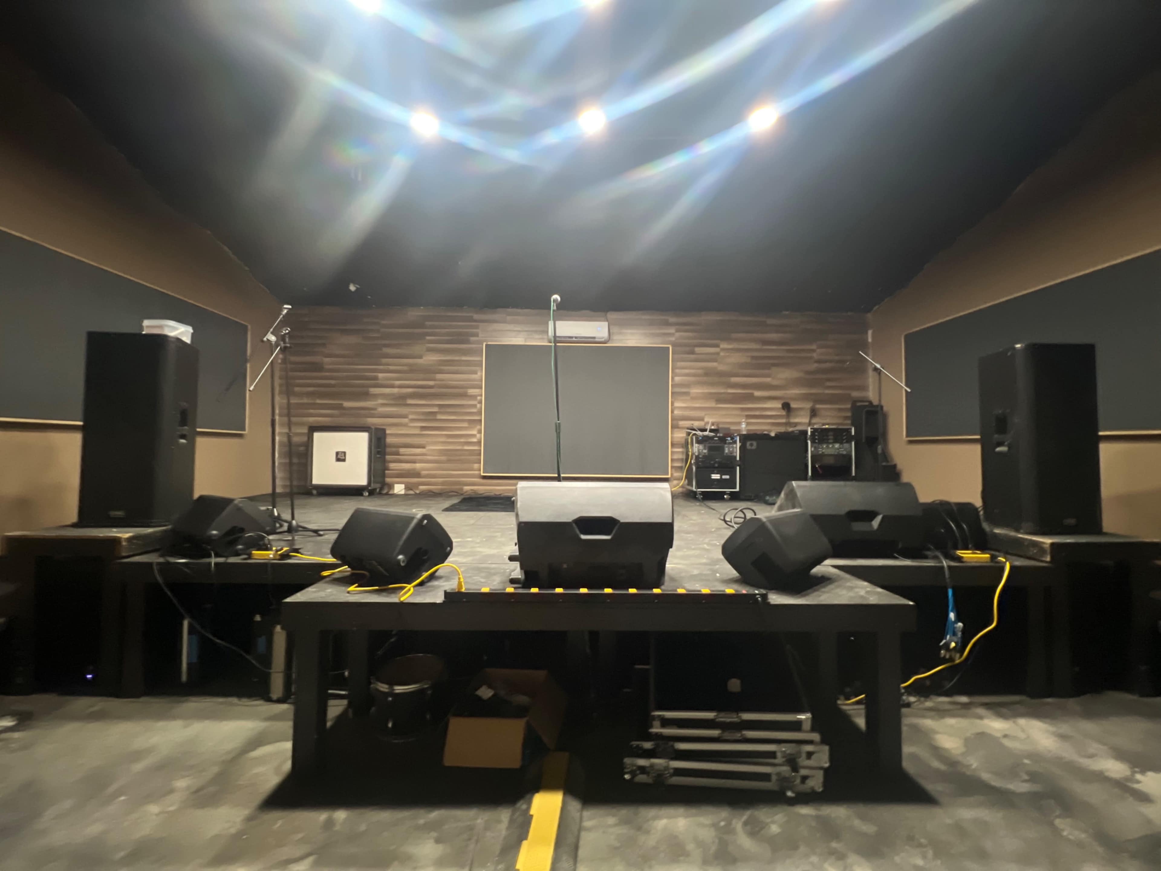 A performance stage with speakers, a microphone stand, and audio equipment in a dimly lit room.