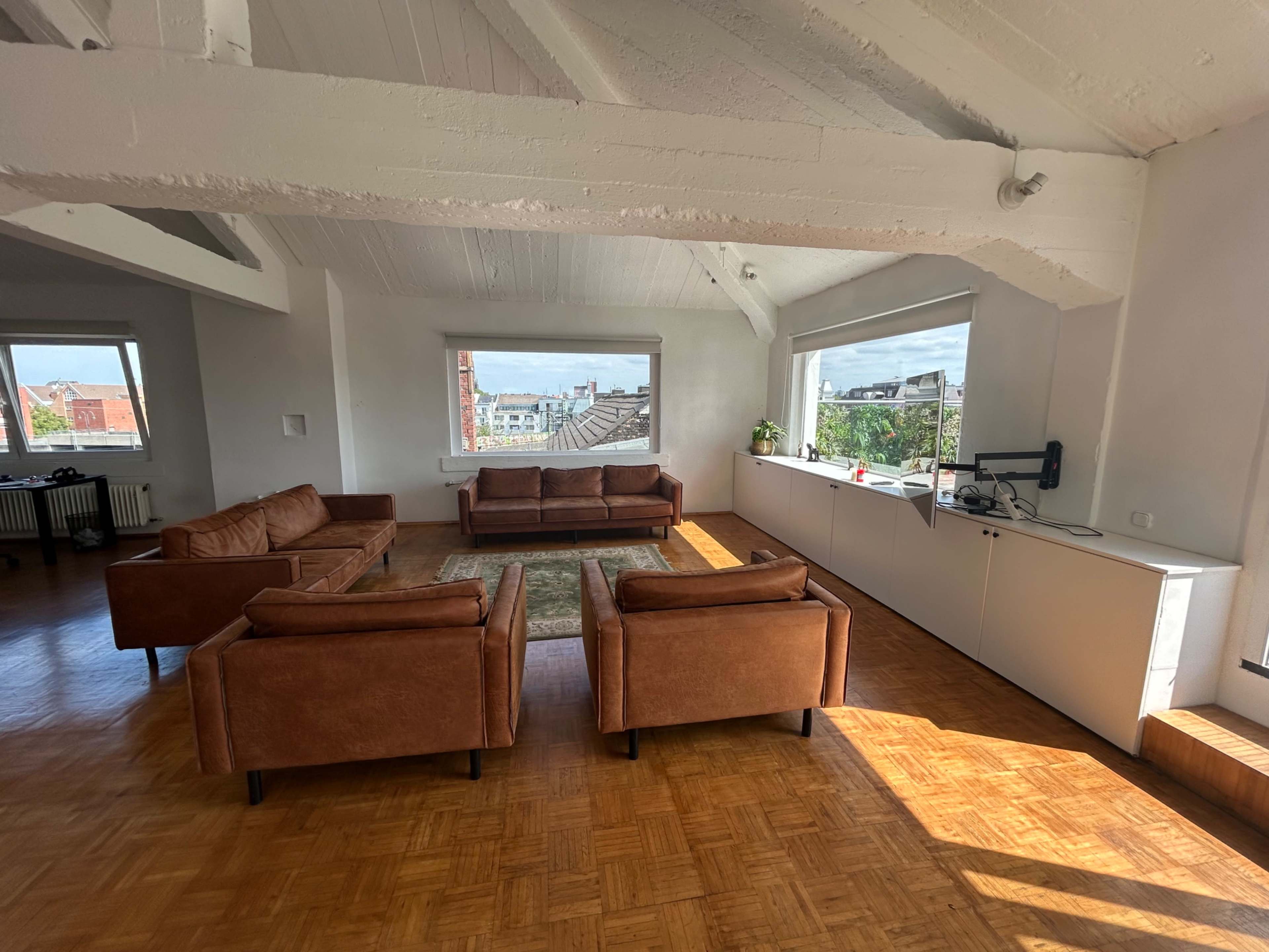 The image shows a spacious room with two brown sofas and a large window providing a view of the outdoors.