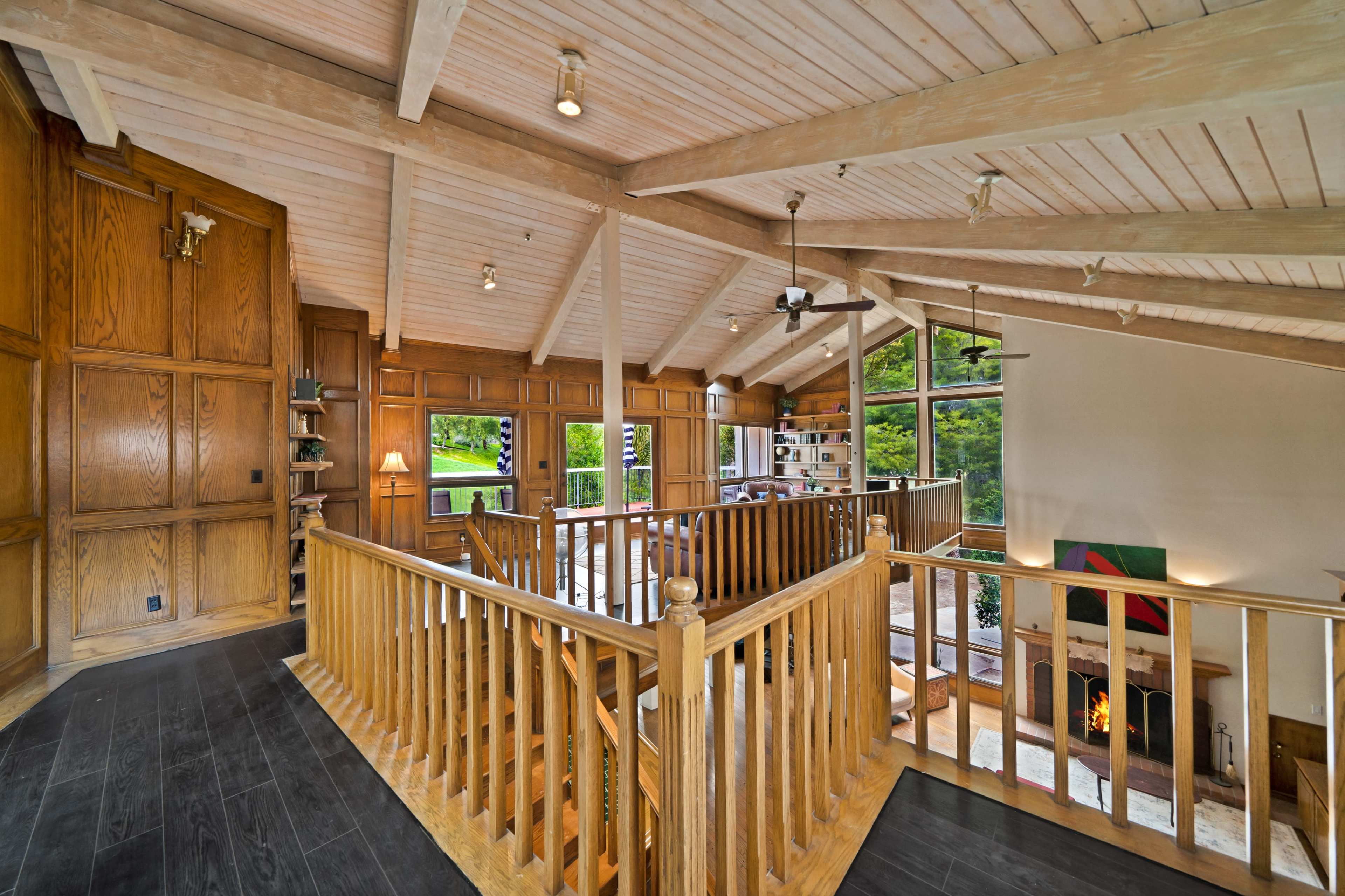 The image shows a spacious interior with wooden railings, vaulted ceilings, and large windows that provide views of the outdoors.