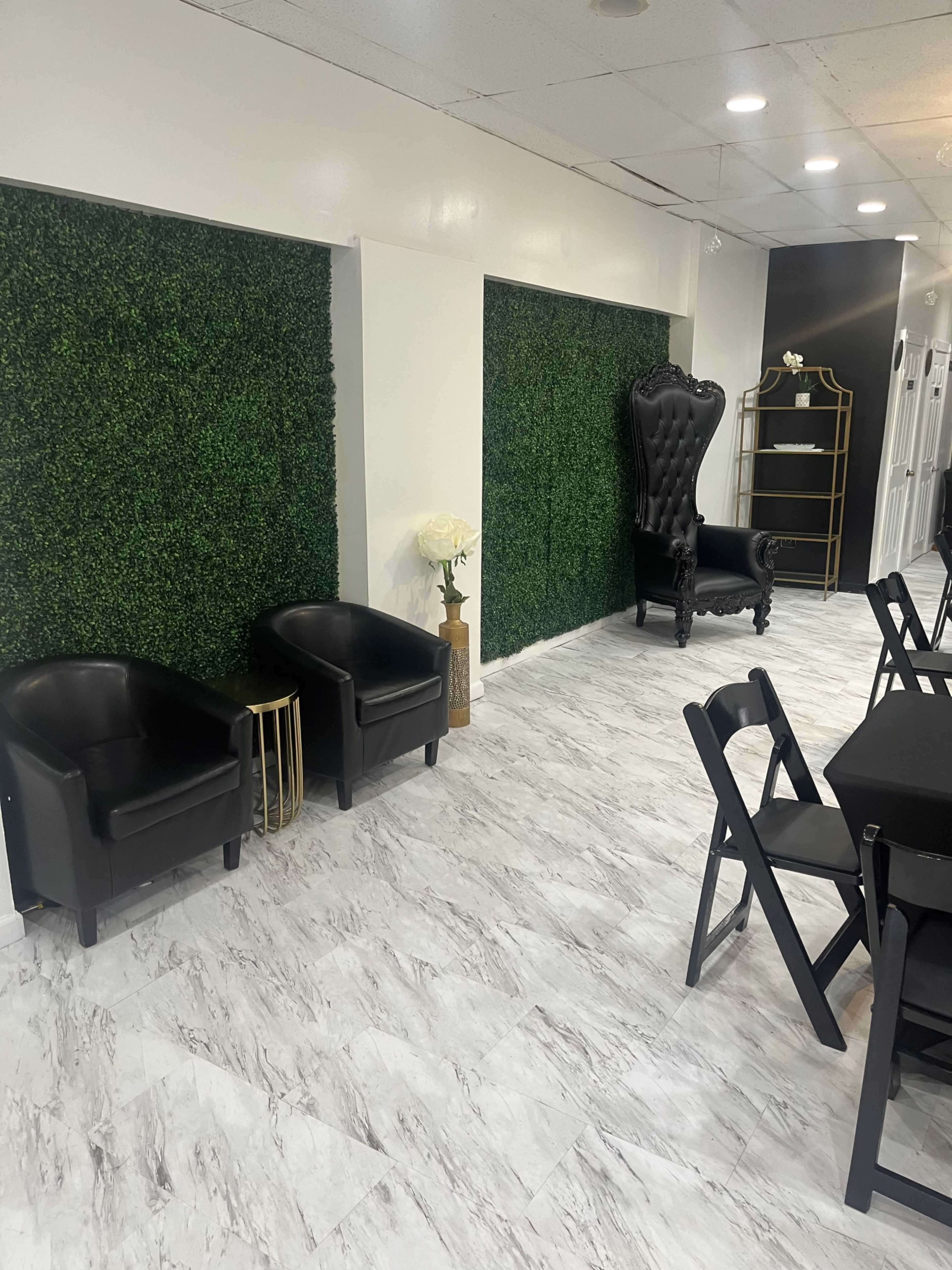 A modern interior space featuring green hedge wall accents, black seating, and a decorative black chair against a white wall.