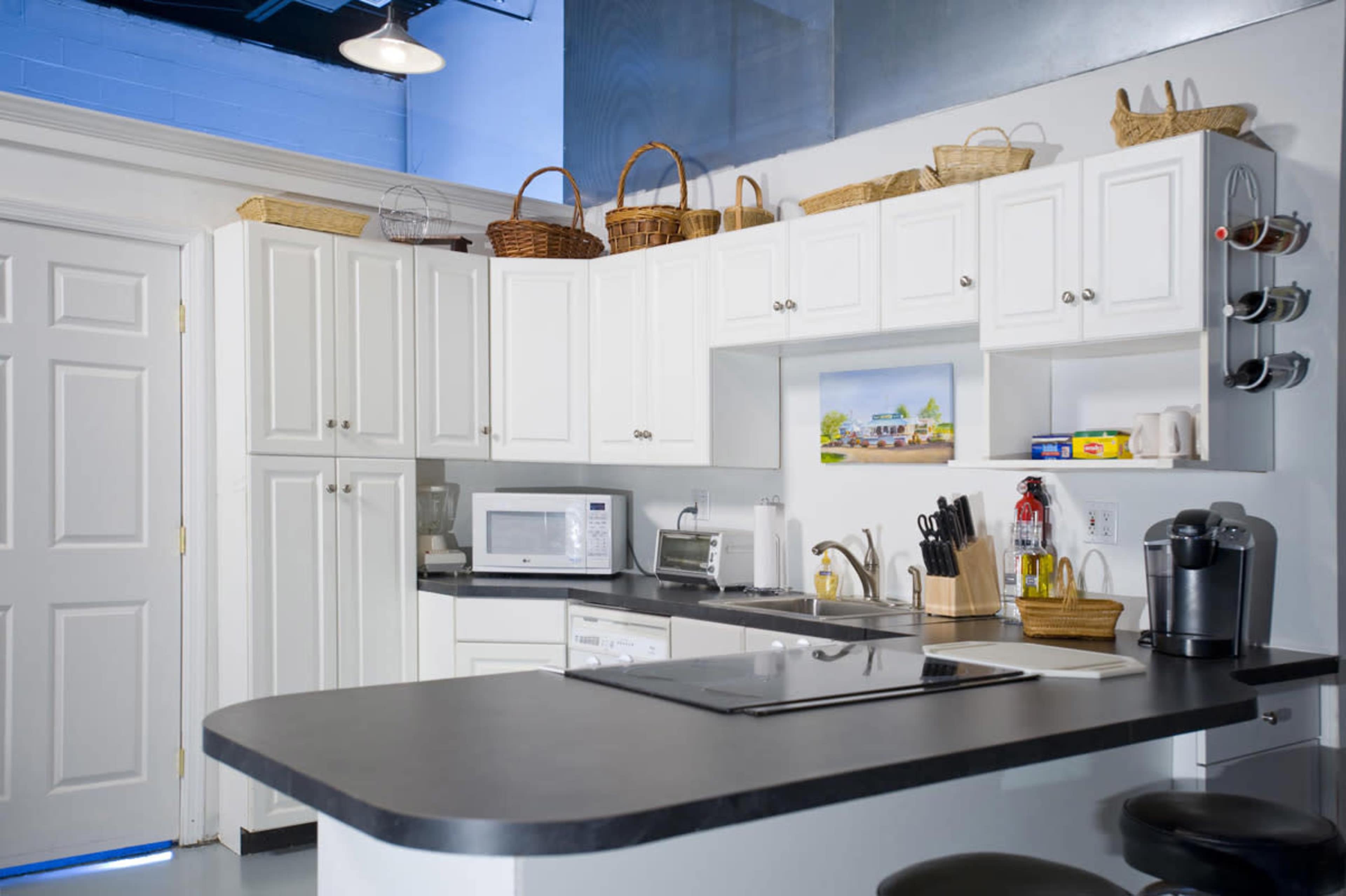 A clean, modern kitchen features white cabinetry, a countertop with appliances, and storage baskets on top.