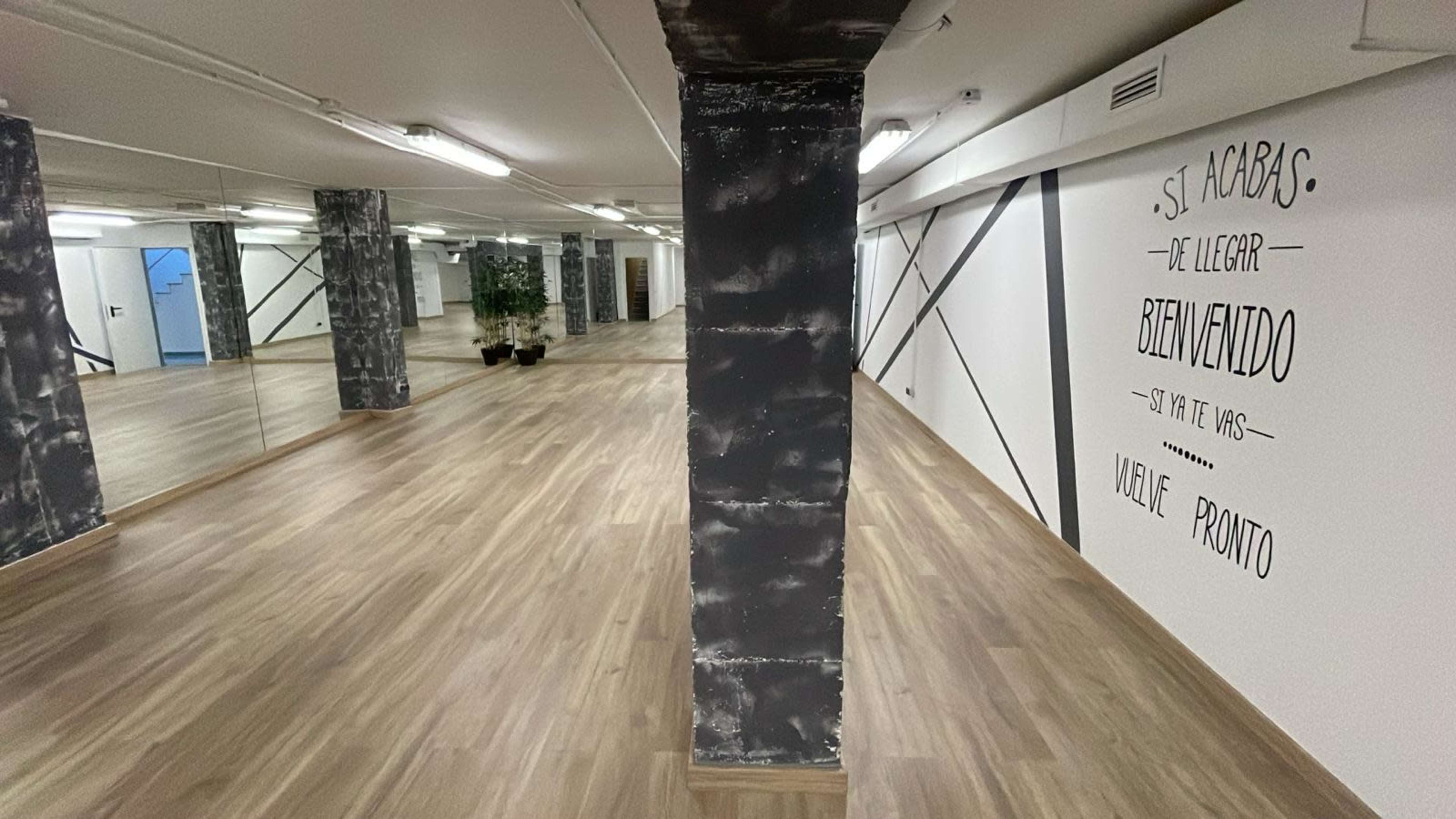 An empty room with wooden flooring, mirrored walls, and a decorative wall featuring text.