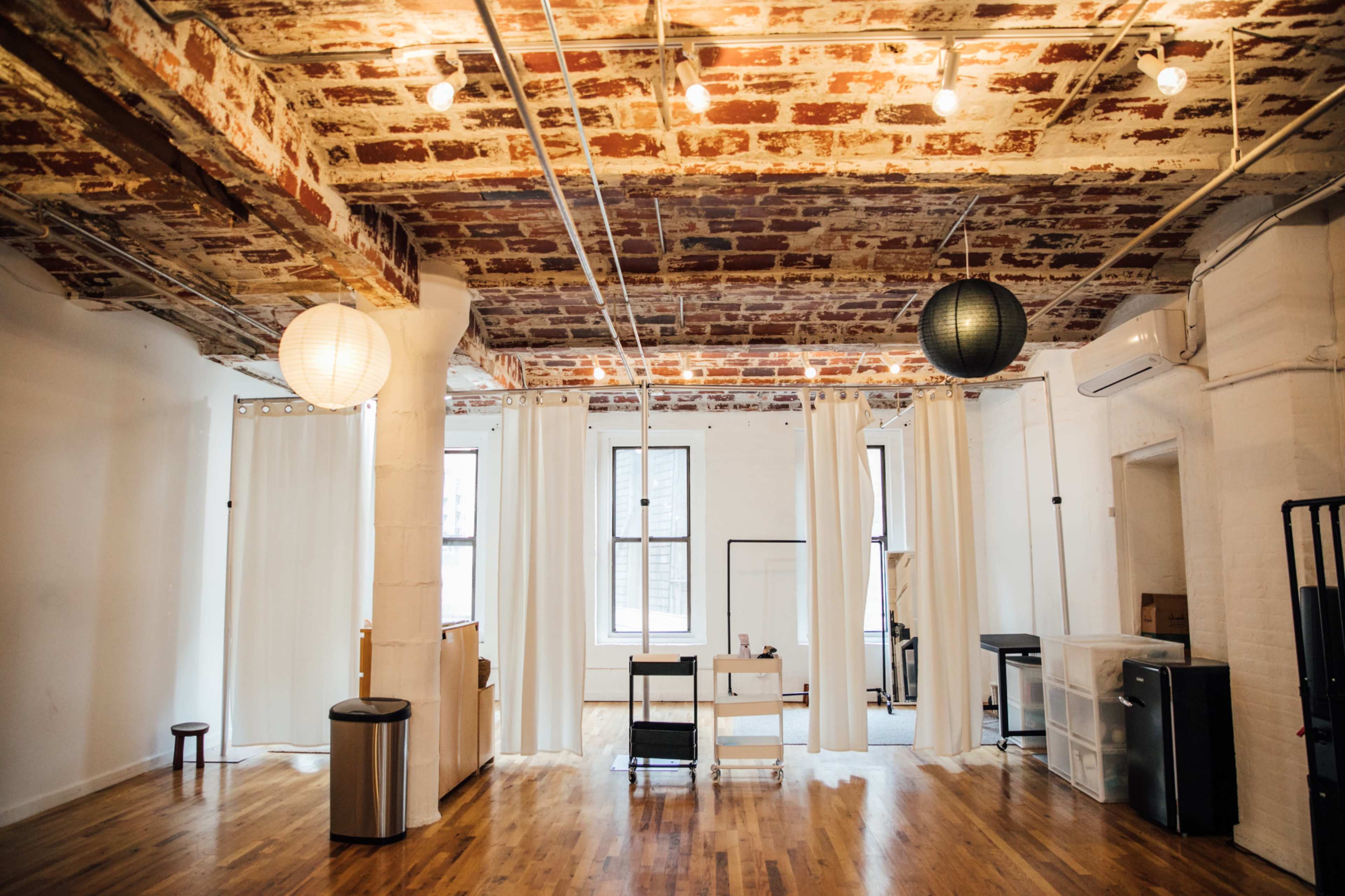 A spacious, minimalistic room with brick ceilings, wooden floors, and soft lighting from pendant lamps.