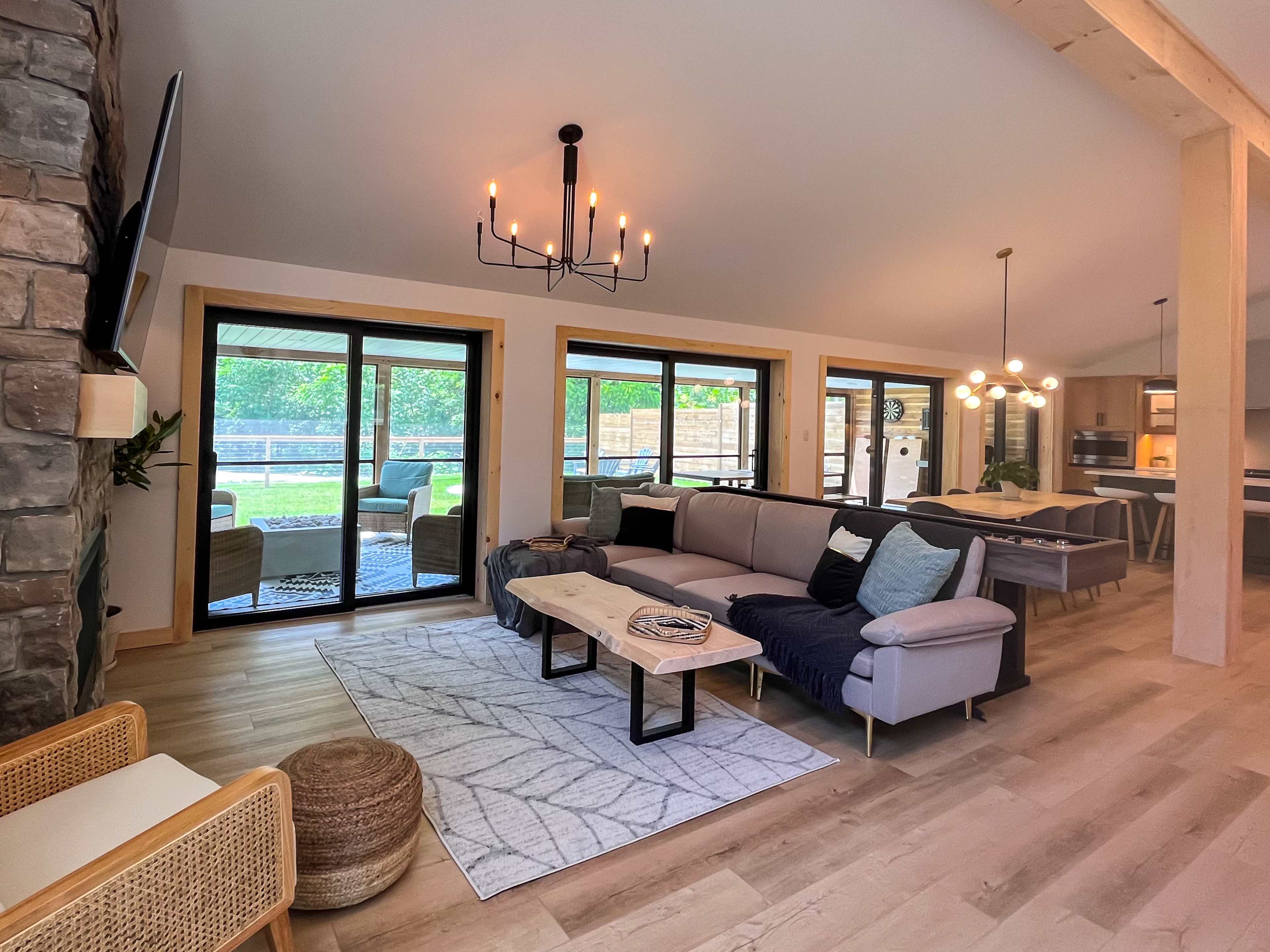 A modern living room featuring a sectional sofa, a wooden coffee table, and large glass doors opening to a green outdoor space.