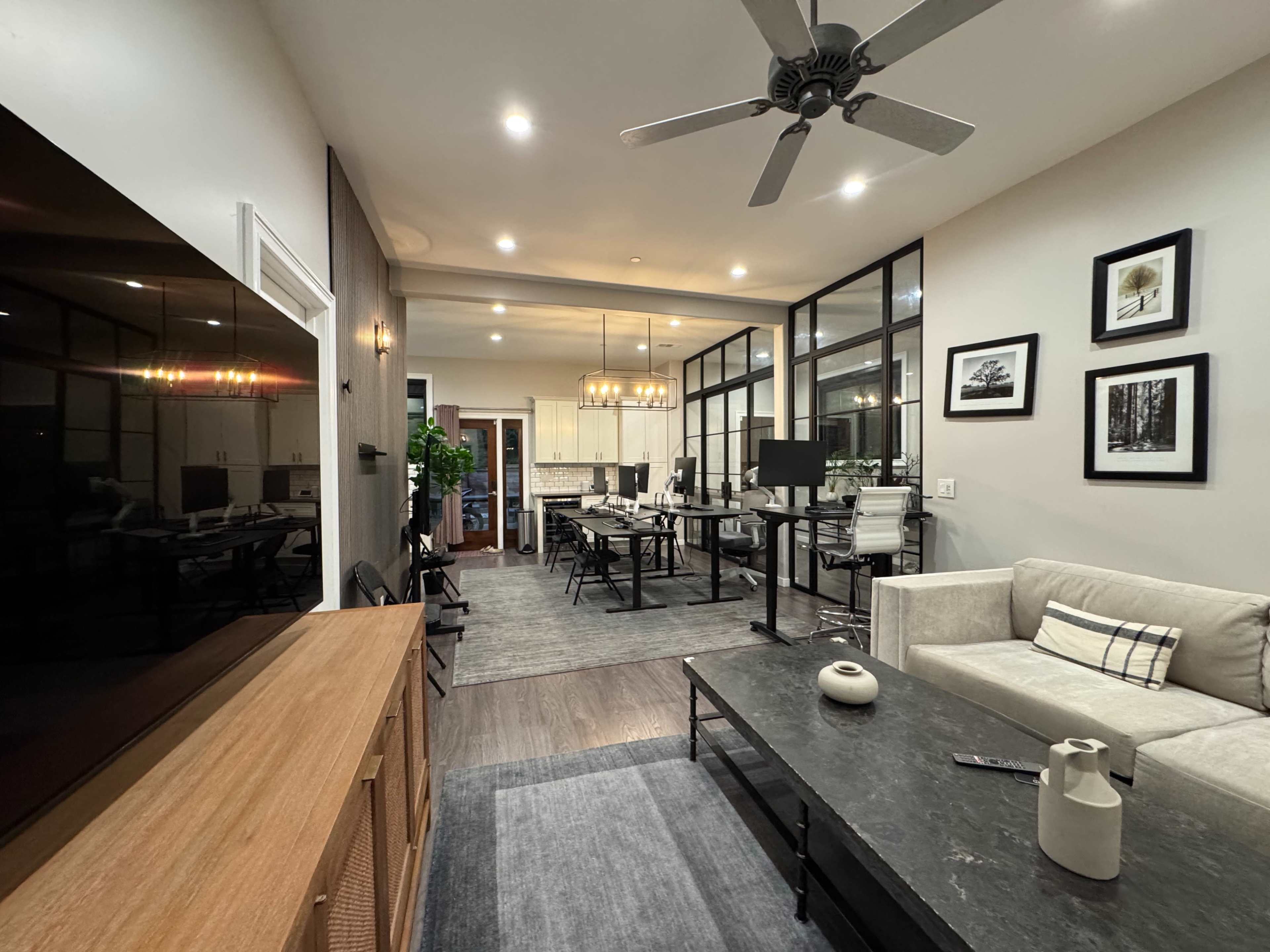 The image shows a modern living room that transitions into a dining area, featuring a neutral color palette, minimalist furniture, and large windows.