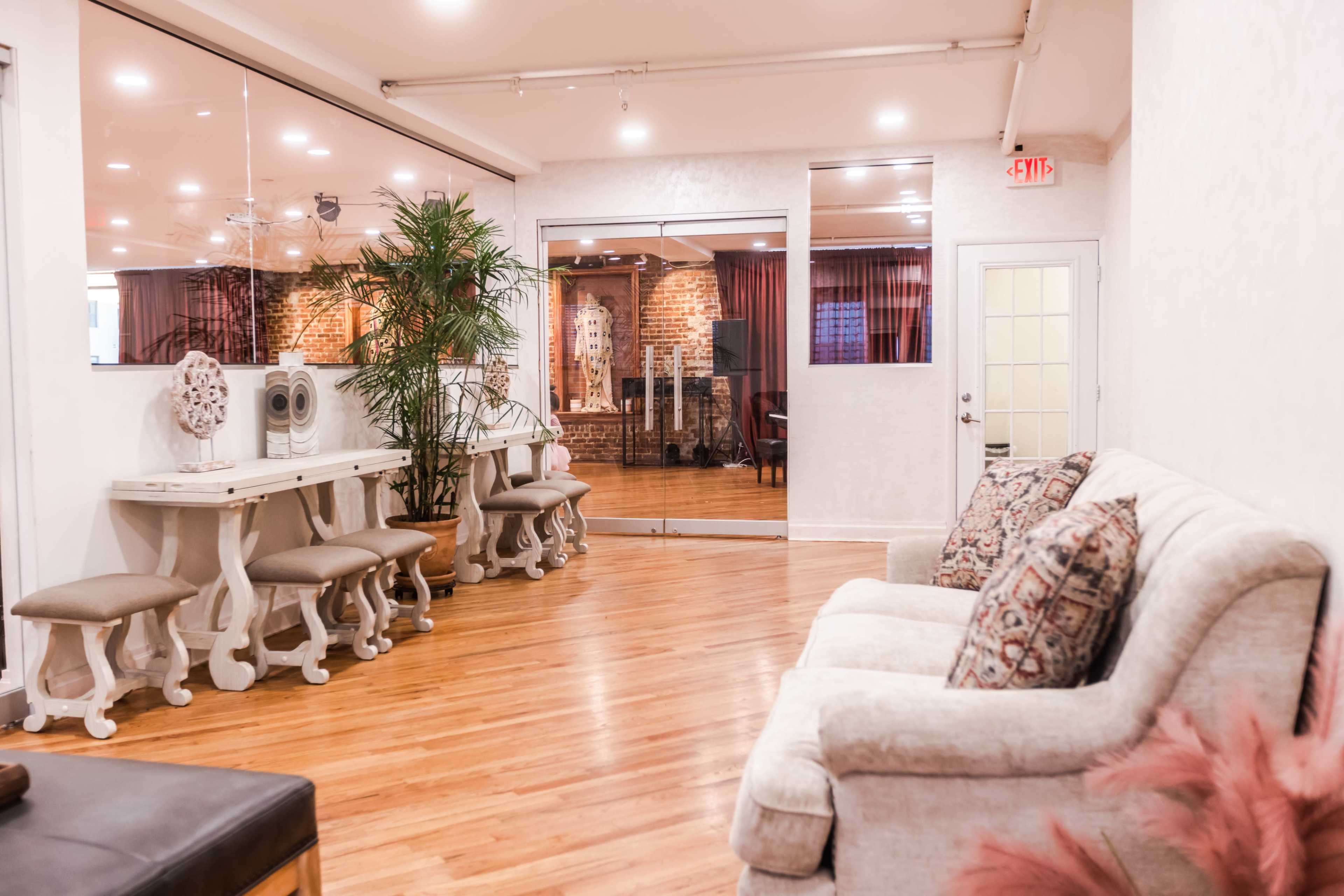 The image shows a spacious interior with a white sofa and a wooden table surrounded by chairs, leading to an open area featuring brick walls and additional seating.