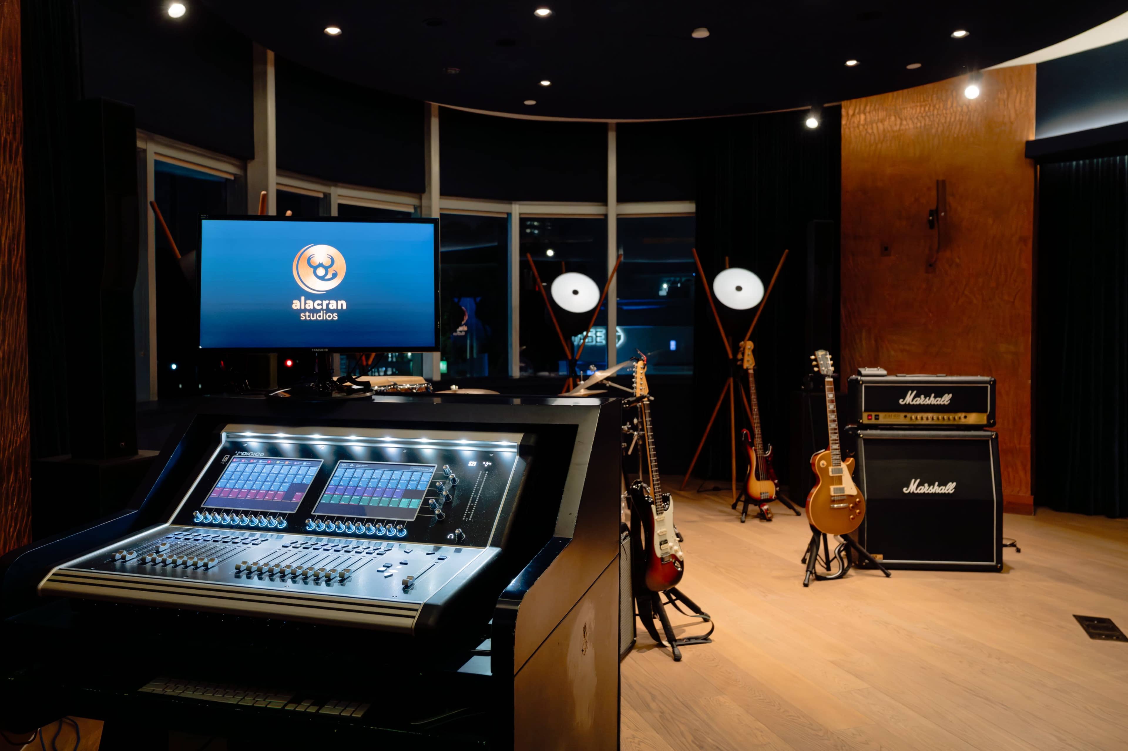 The image features a modern music studio with a digital mixing console, various guitars on stands, and a large amplifier against the wall.