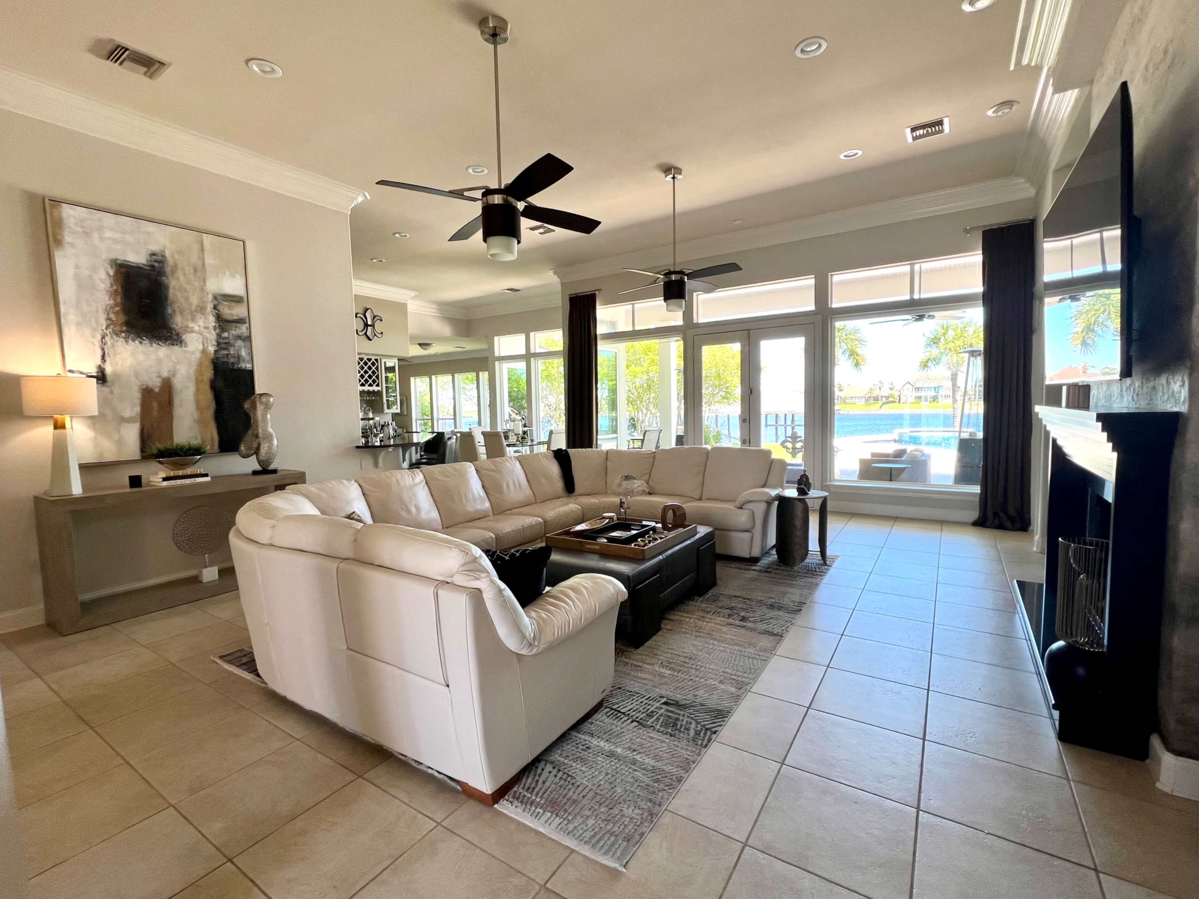 A modern living room featuring a large sectional sofa, a coffee table, and large windows that open to a view of a pool and outdoor area.