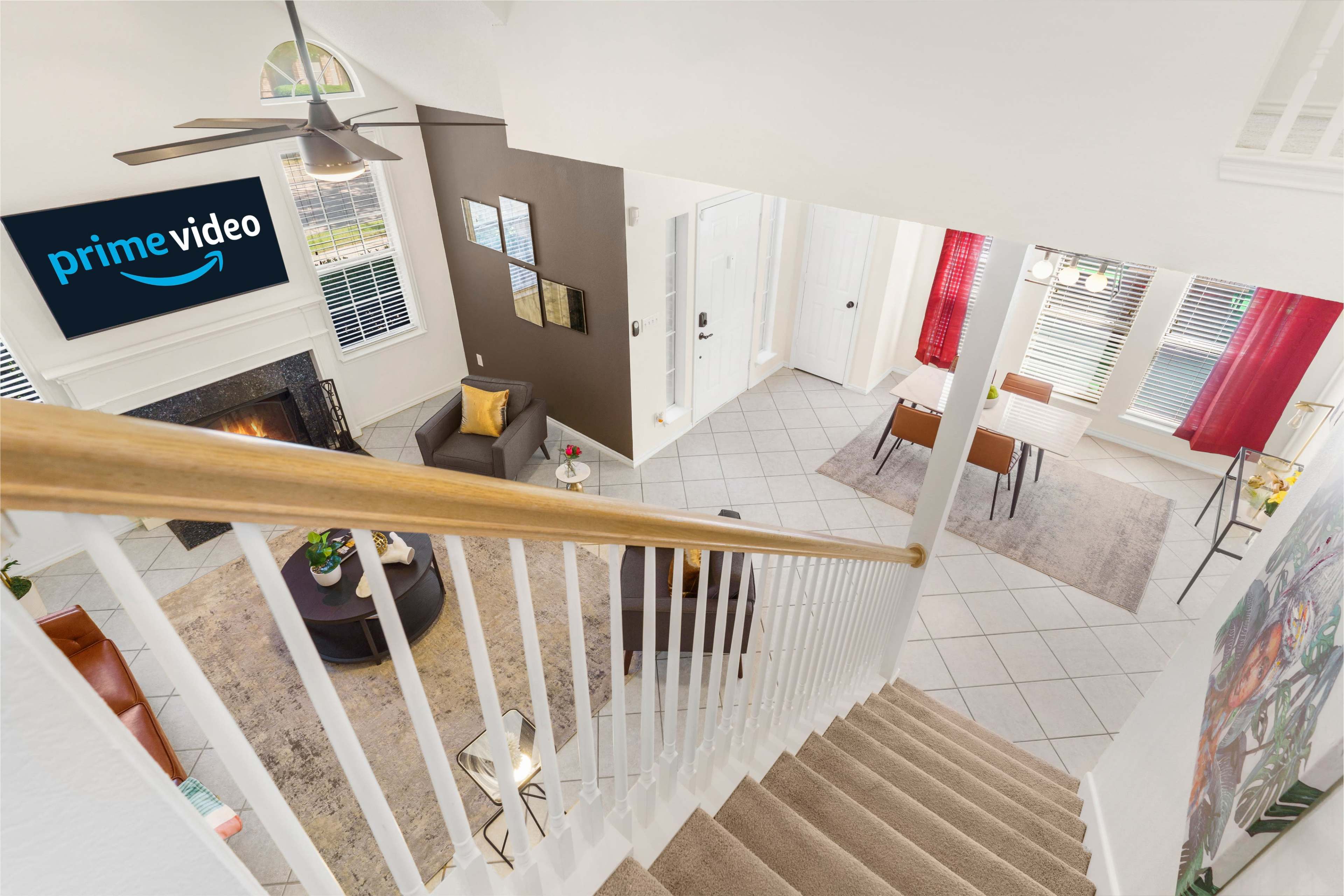 A view from the top of a staircase overlooking a living area with a large TV displaying the Prime Video logo and a dining space with a table and chairs.