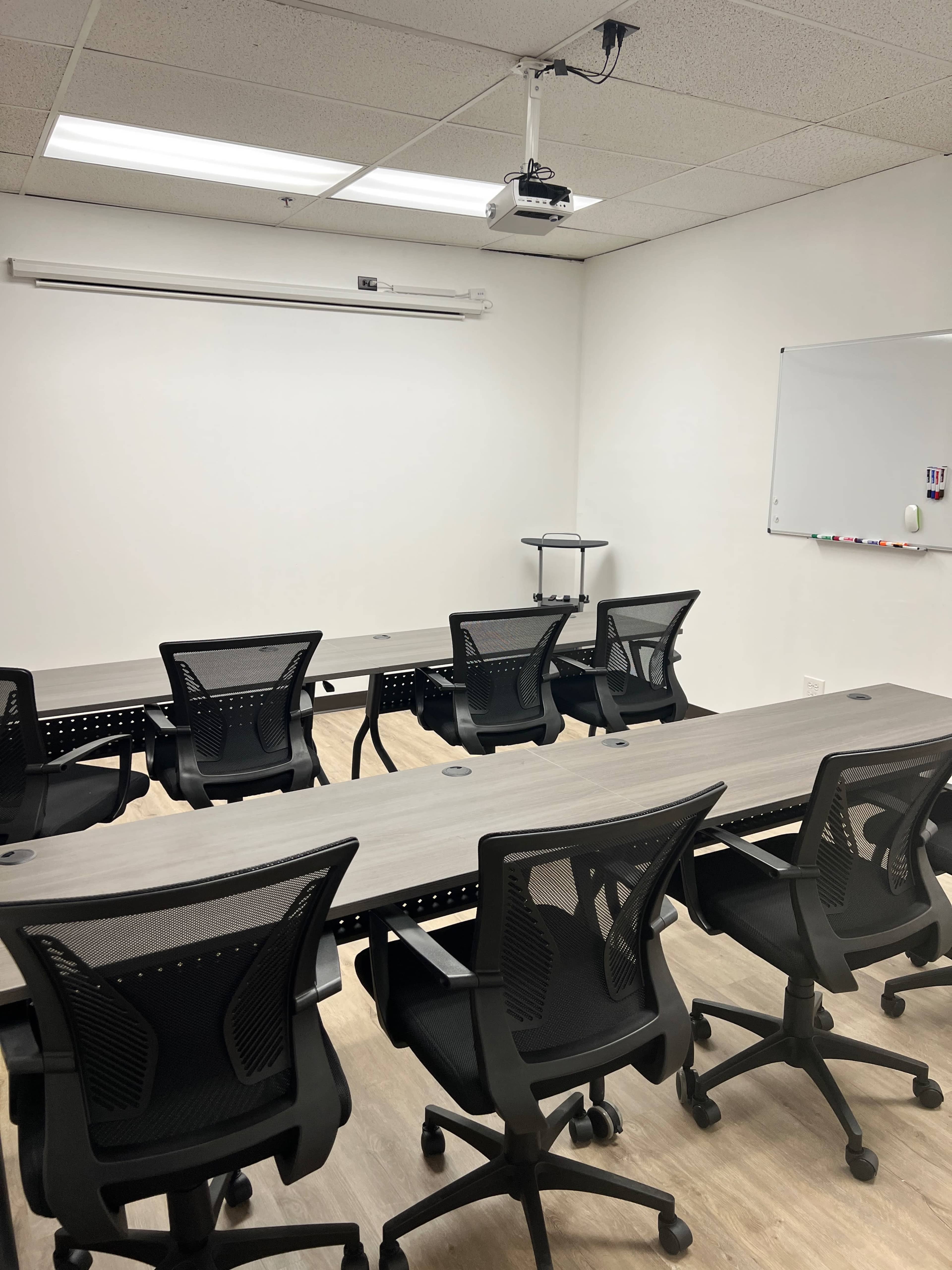 A modern conference room with a long table and several black office chairs arranged around it, featuring a white wall for presentations and a whiteboard.