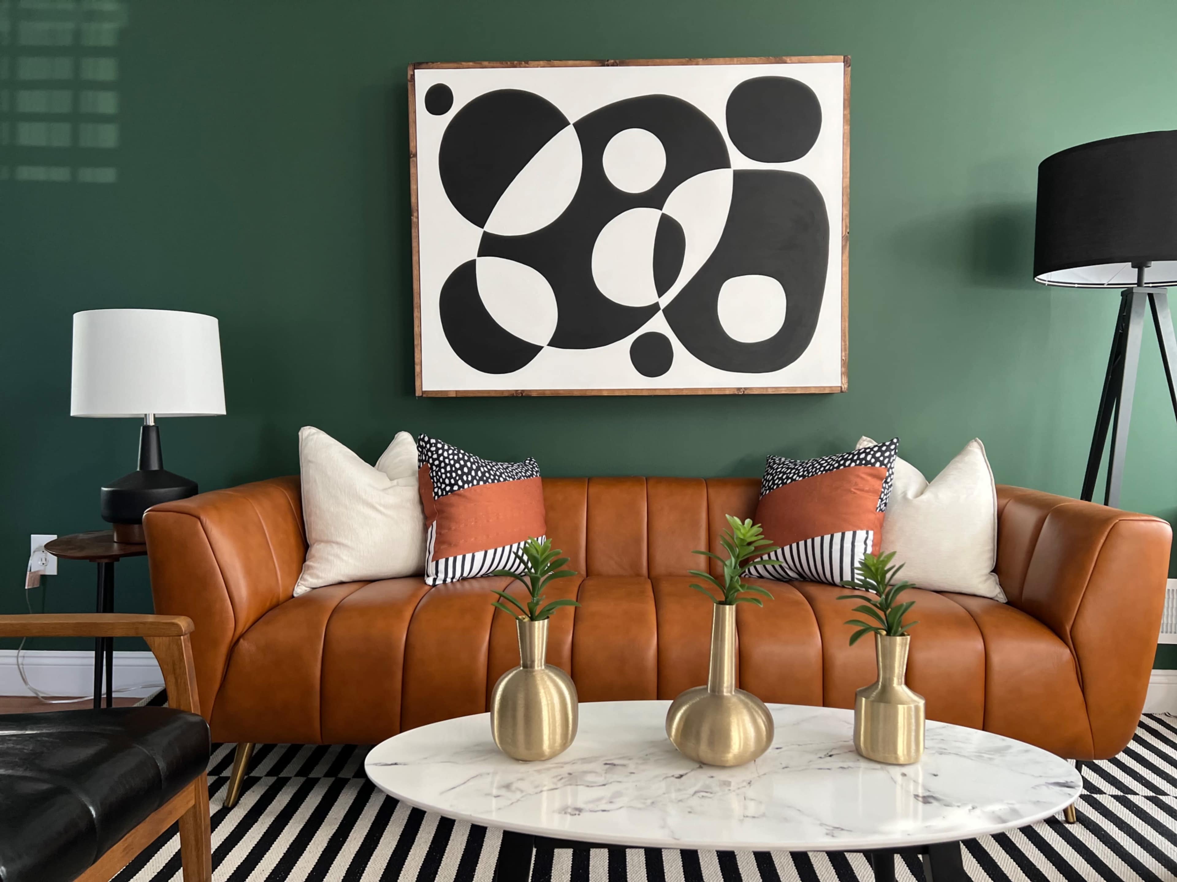 The image depicts a modern living room with a brown leather sofa, decorative pillows, a round marble coffee table, and abstract artwork on a green wall.