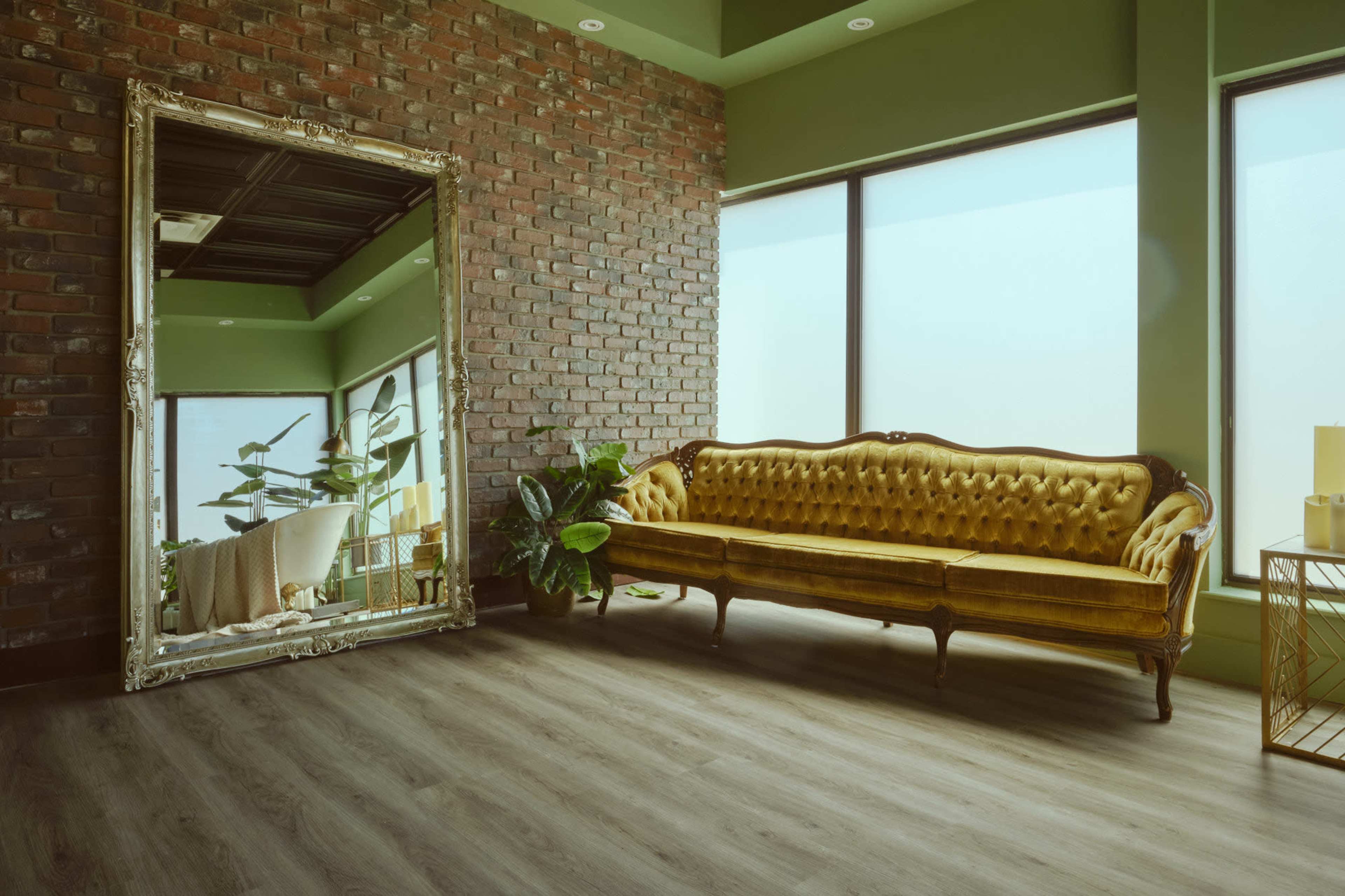 The image features a bright room with green walls, a vintage-style yellow tufted sofa, a large ornate mirror, and plants near a window.