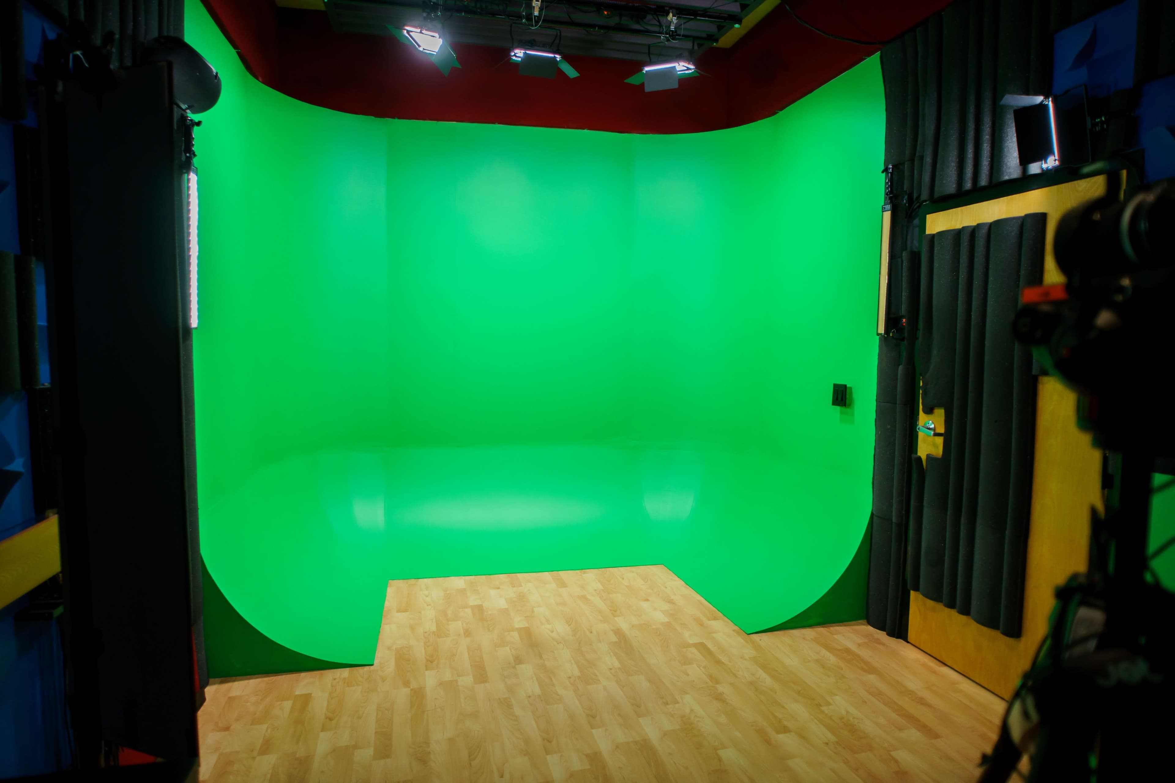 A green screen backdrop inside a studio, with wooden flooring and overhead lighting.