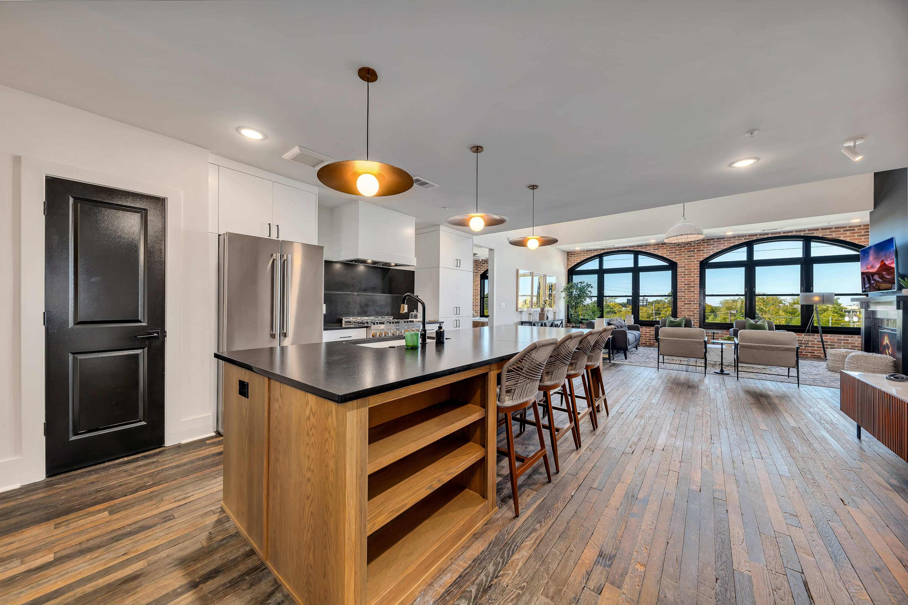 A modern kitchen and living area featuring an island with bar stools, stainless steel appliances, and large arched windows that provide natural light.