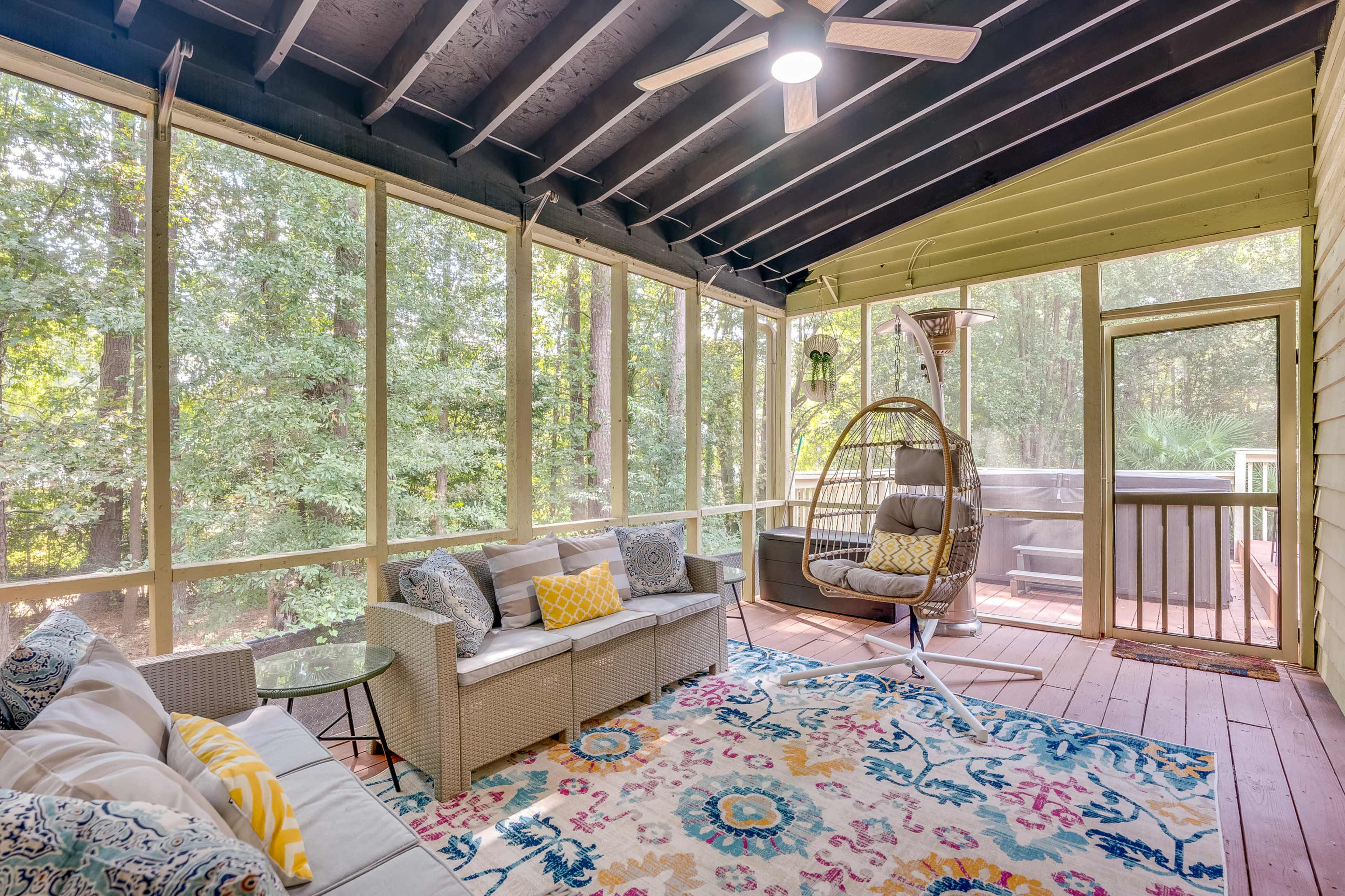 The image shows a screened-in porch with a sofa, a hanging chair, and a table, surrounded by trees and decorated with a colorful rug.