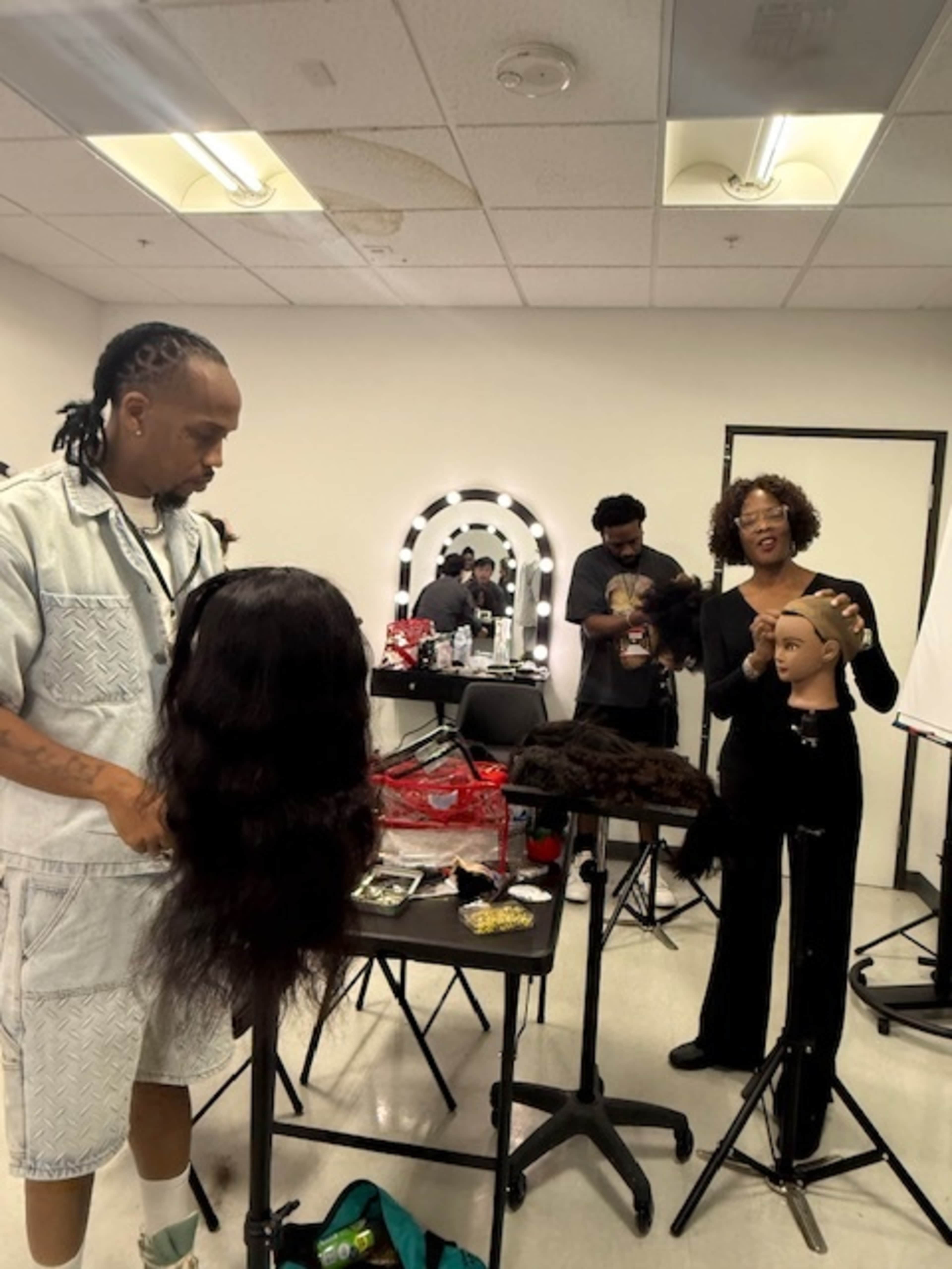 In a well-lit room, a hairstyling class is taking place with instructors and students working on mannequin heads.