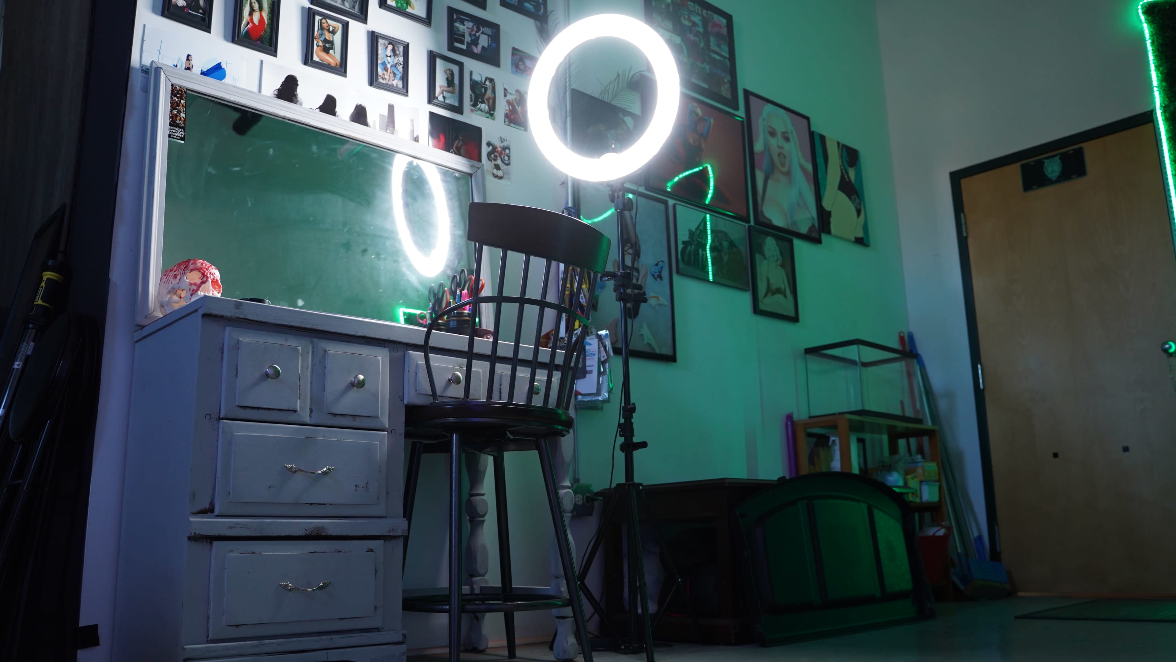 A makeup vanity with a circular light and a chair in a room adorned with various framed photographs on the walls.