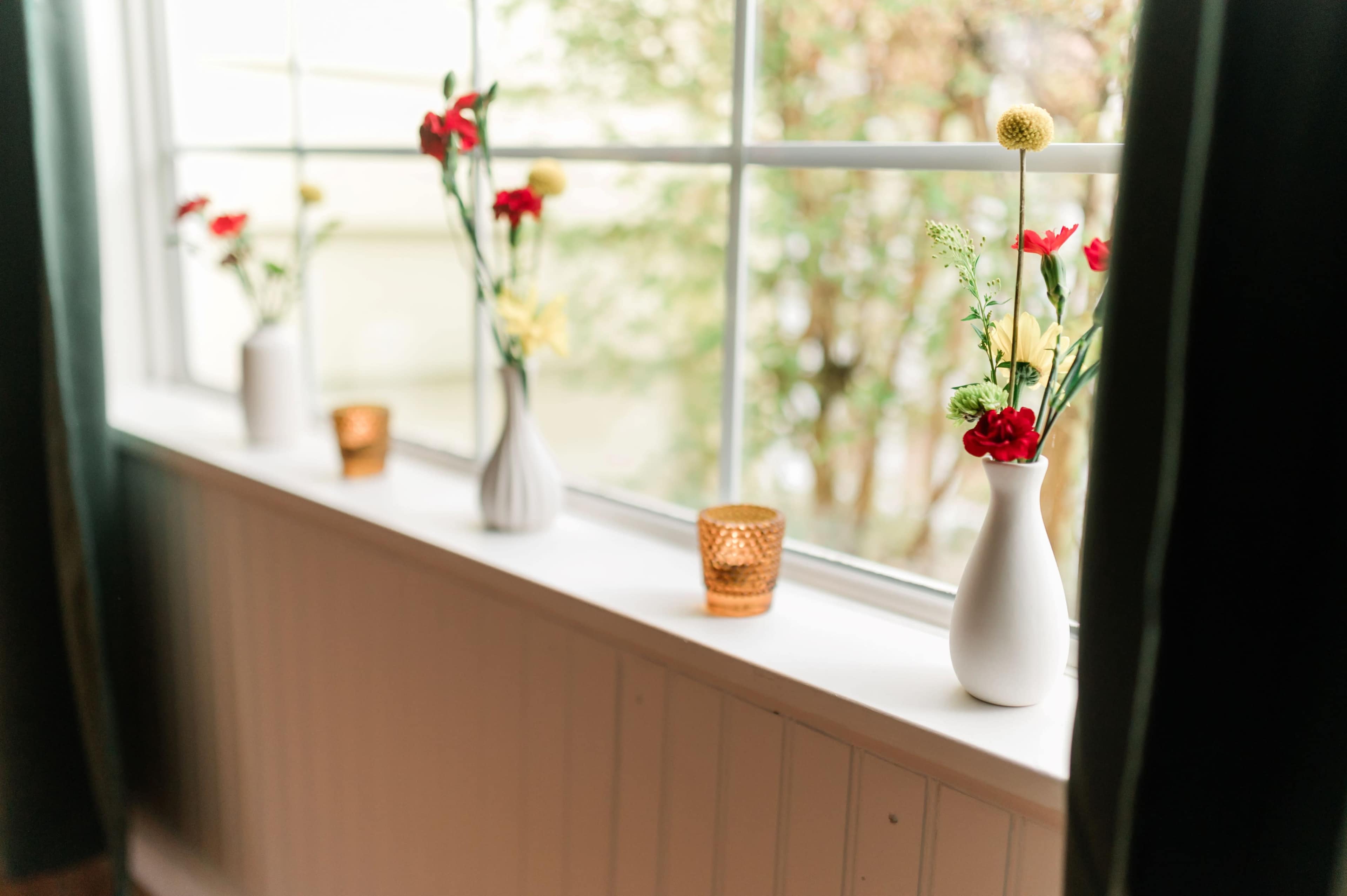 The image shows a window sill decorated with vases containing flowers and small candle holders.