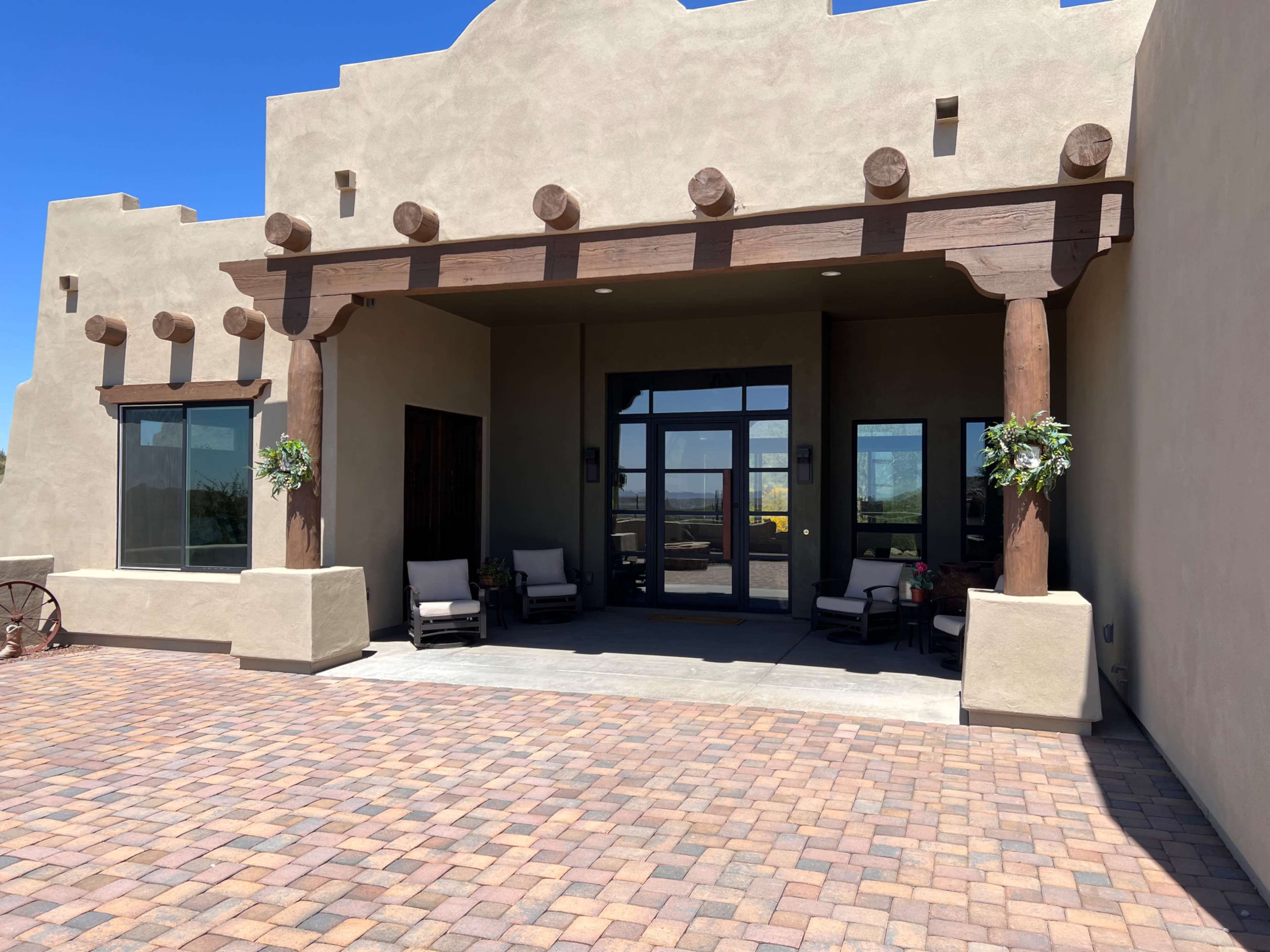 A southwestern-style building entrance with wooden beams and stone accents, featuring two chairs and potted plants.