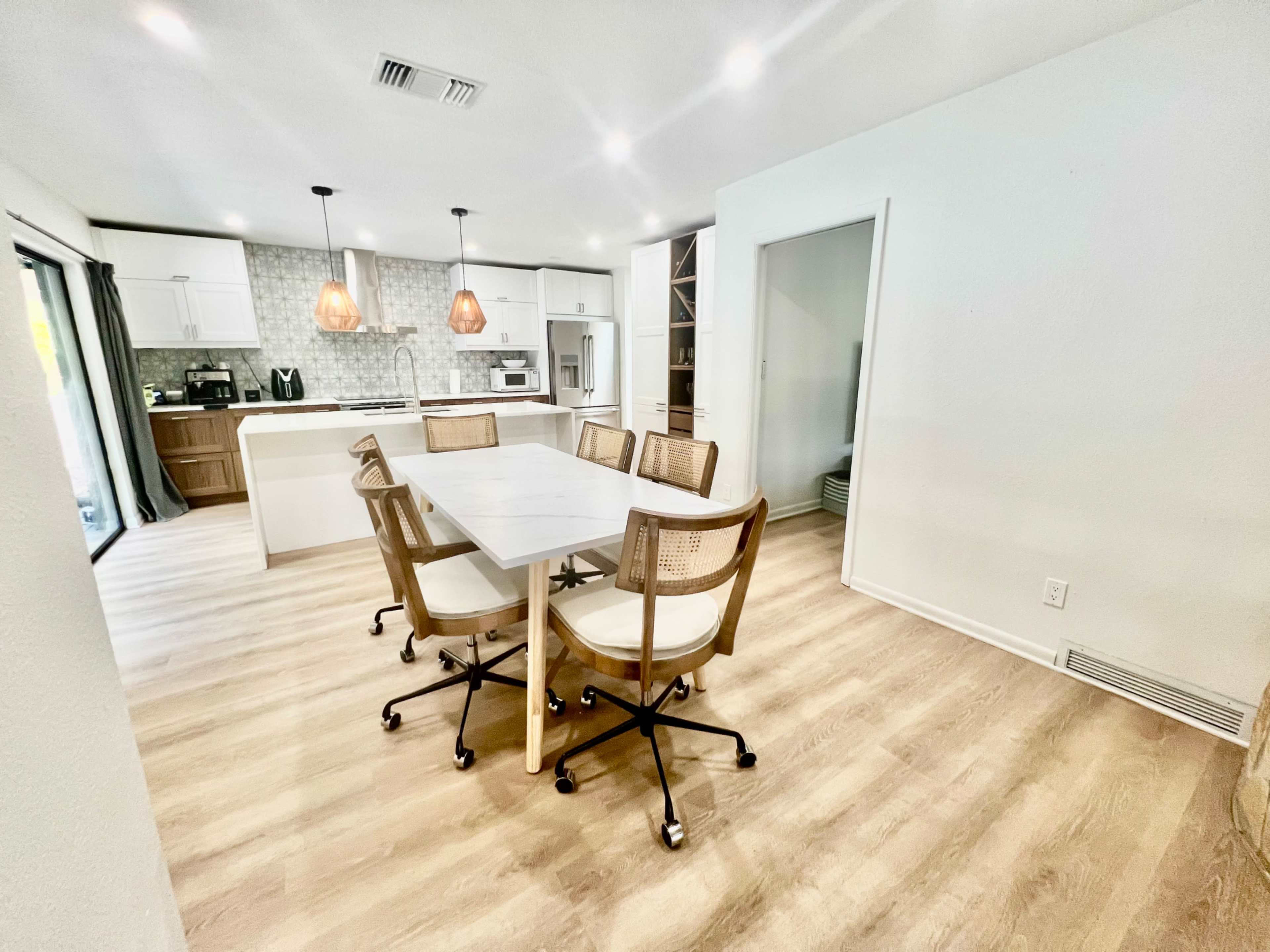 A spacious dining area features a large table surrounded by six chairs, with a modern kitchen visible in the background.