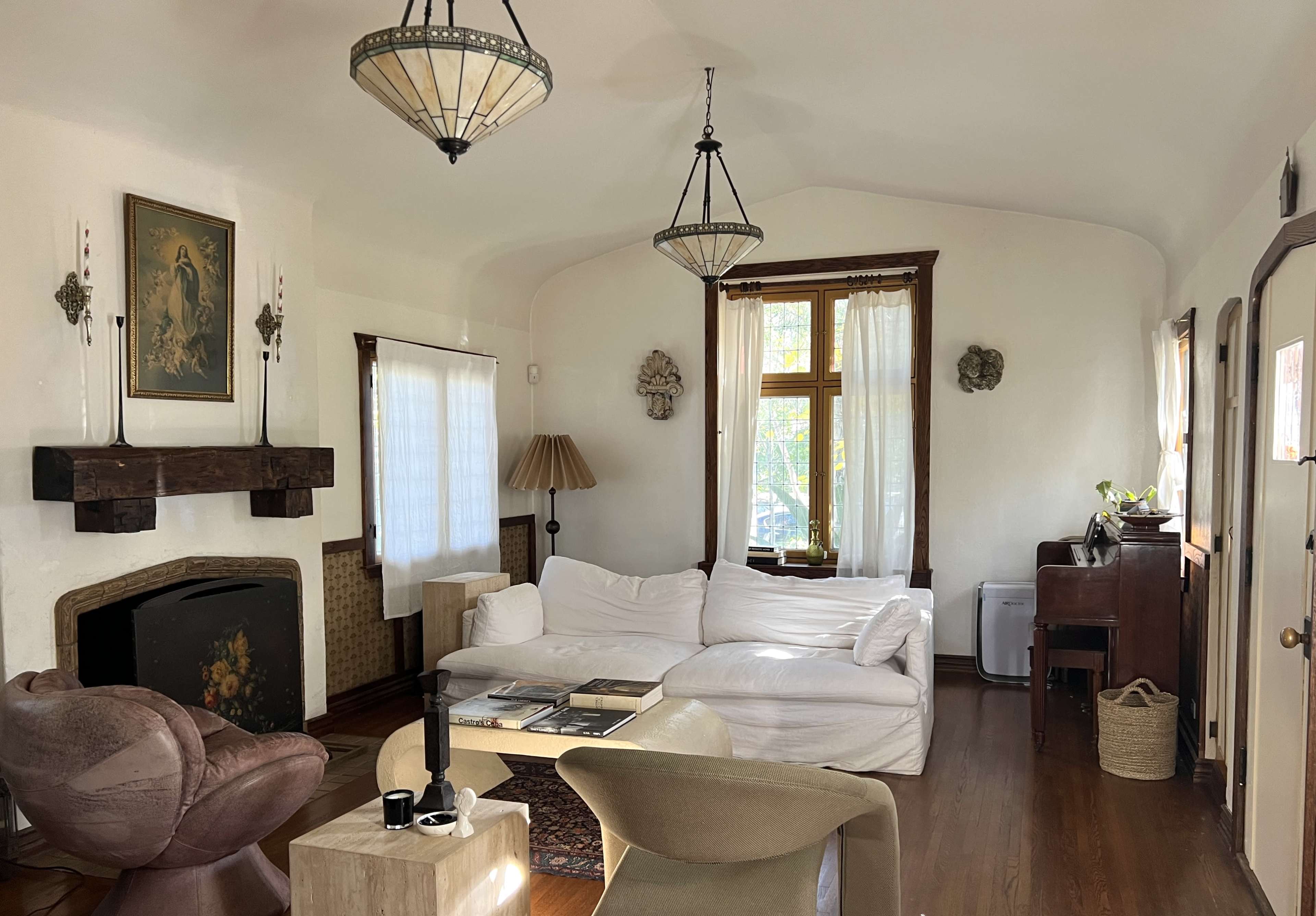 The image shows a cozy living room with a white sofa, a wooden mantel with a painting above it, and various warm lighting fixtures.