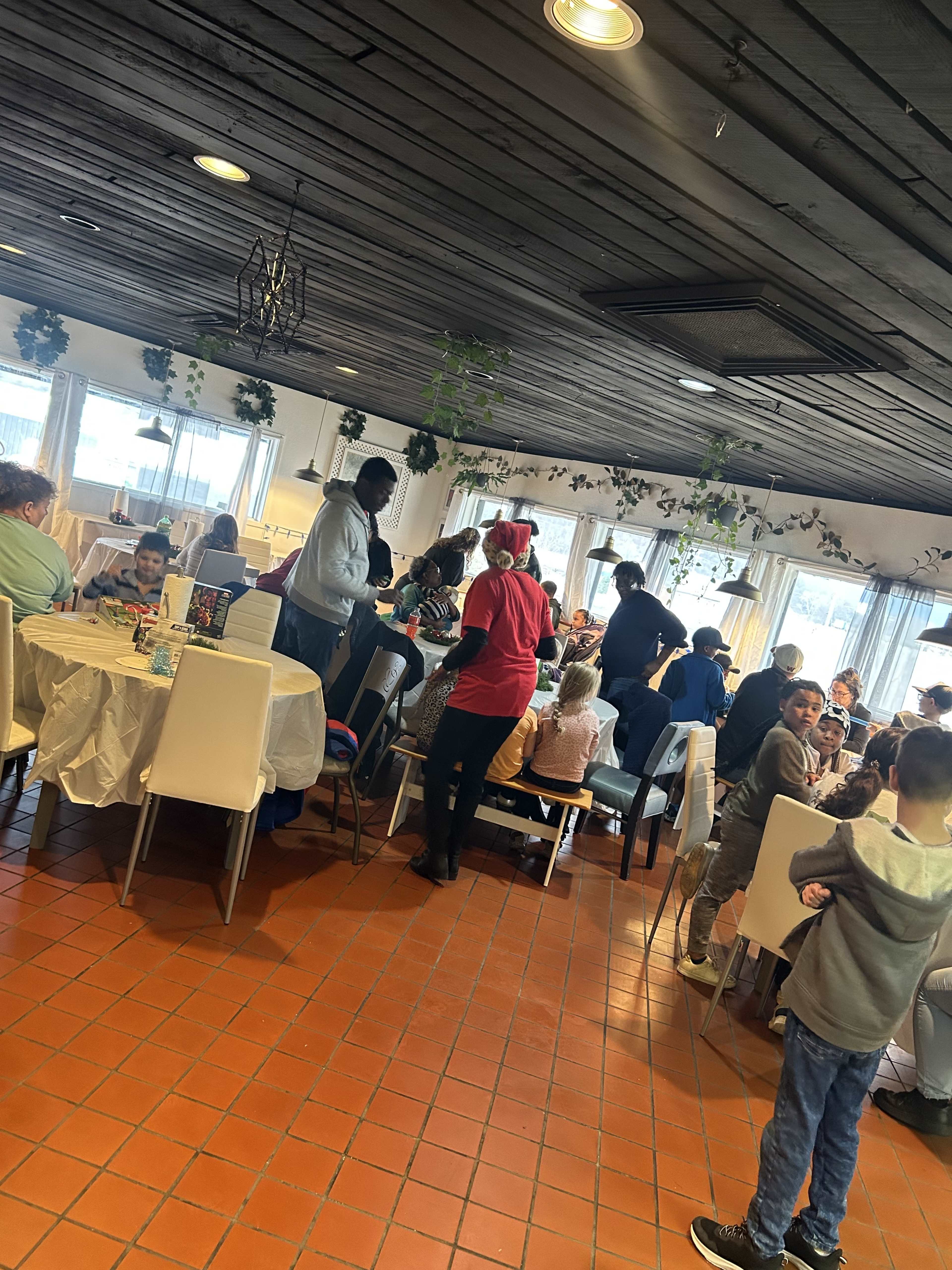 The image shows a busy restaurant interior with many families seated at tables, some children playing, while staff members attend to guests.