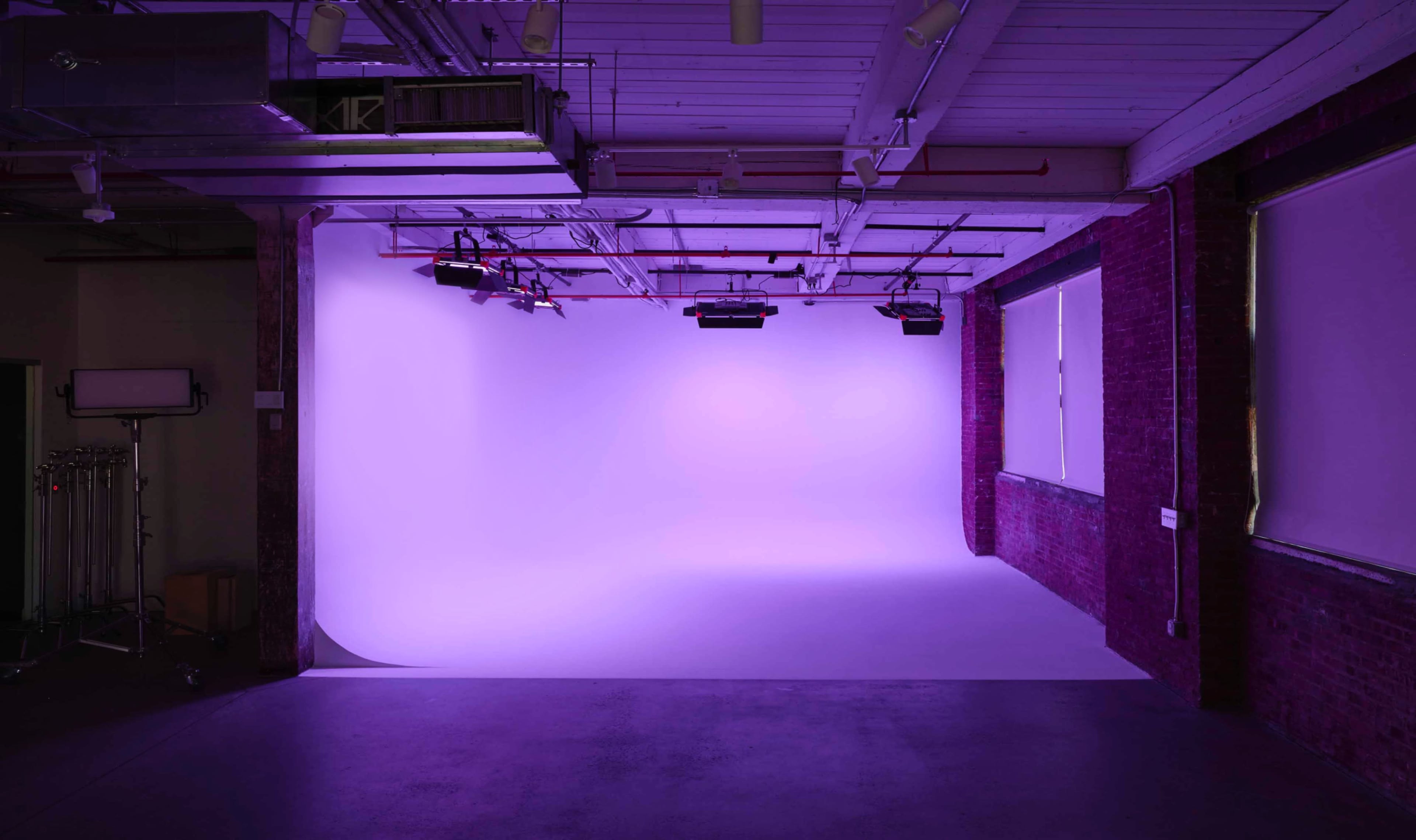 The image shows a spacious studio with a smooth purple backdrop and exposed brick walls.