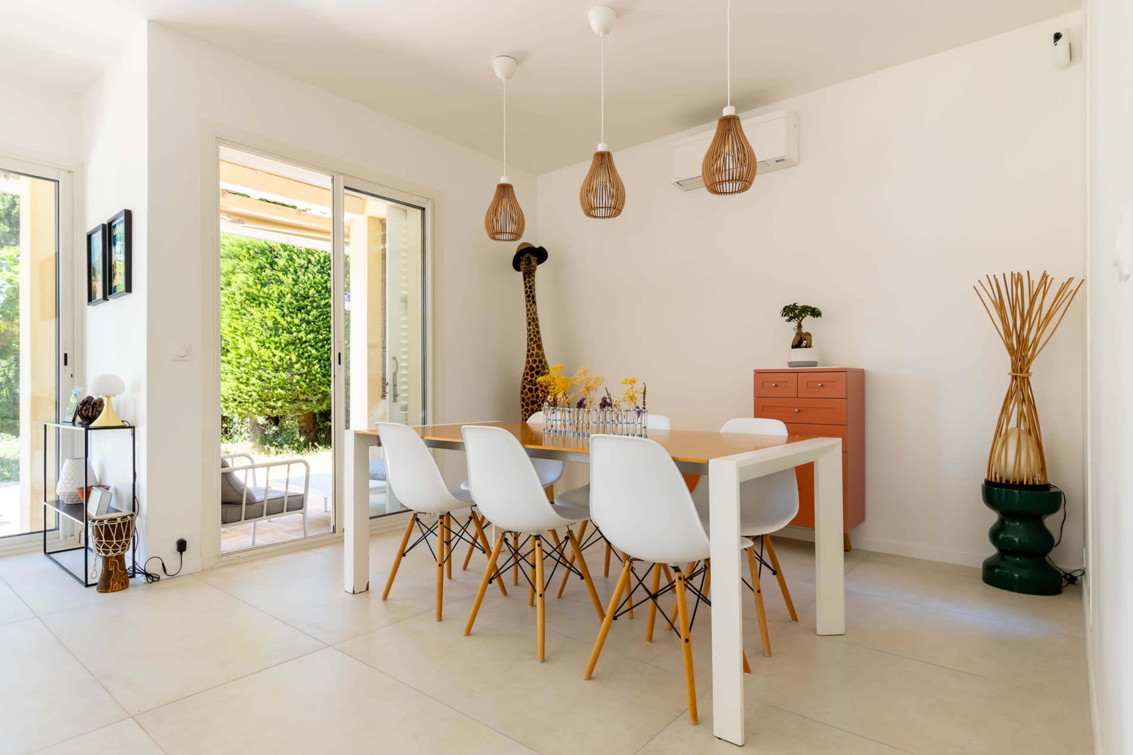 A modern dining area features a white table with six chairs, decorative items, and large glass doors leading to a garden.