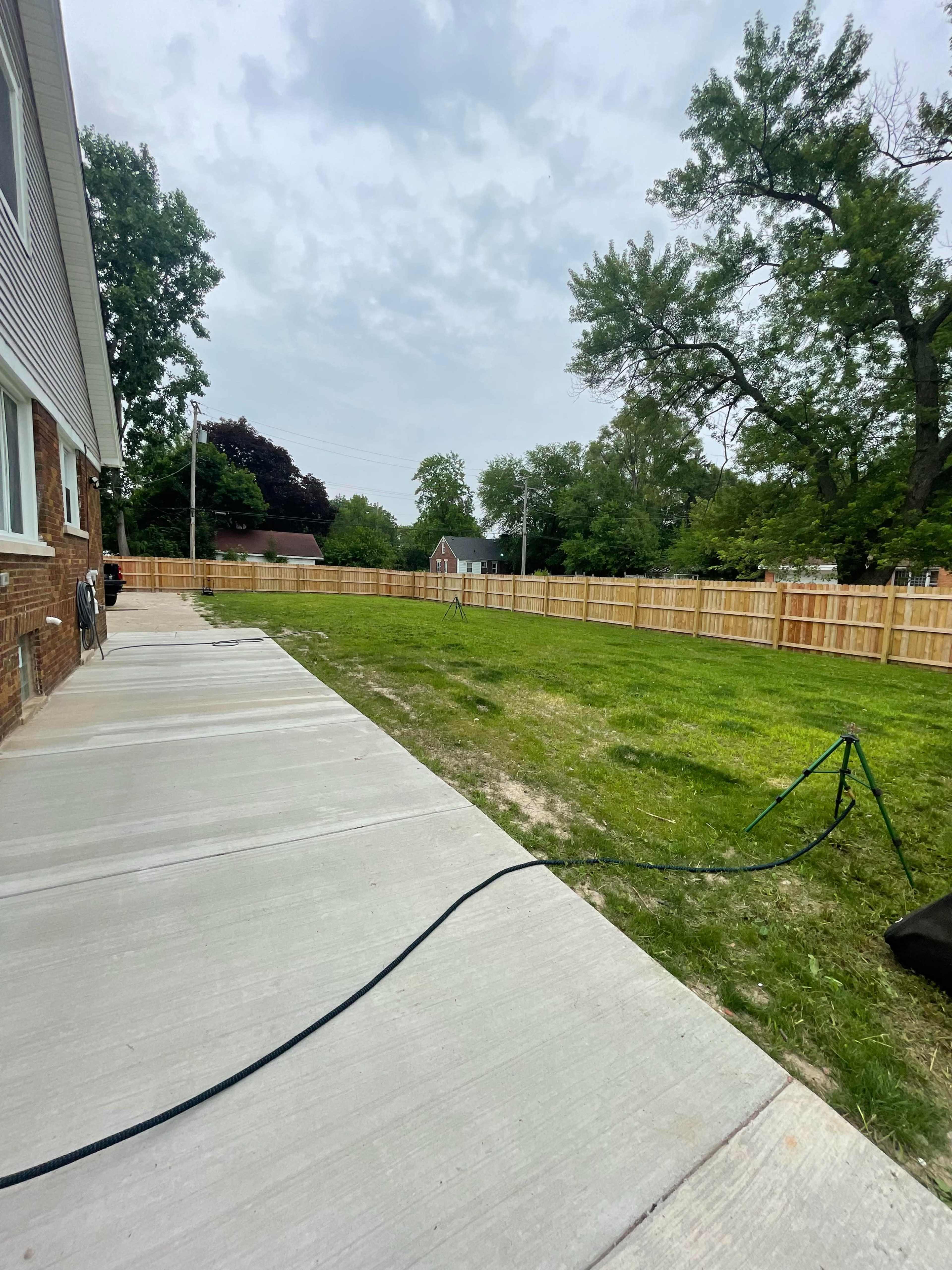 A grassy yard is enclosed by a wooden fence, with a concrete pathway leading to the house on one side.