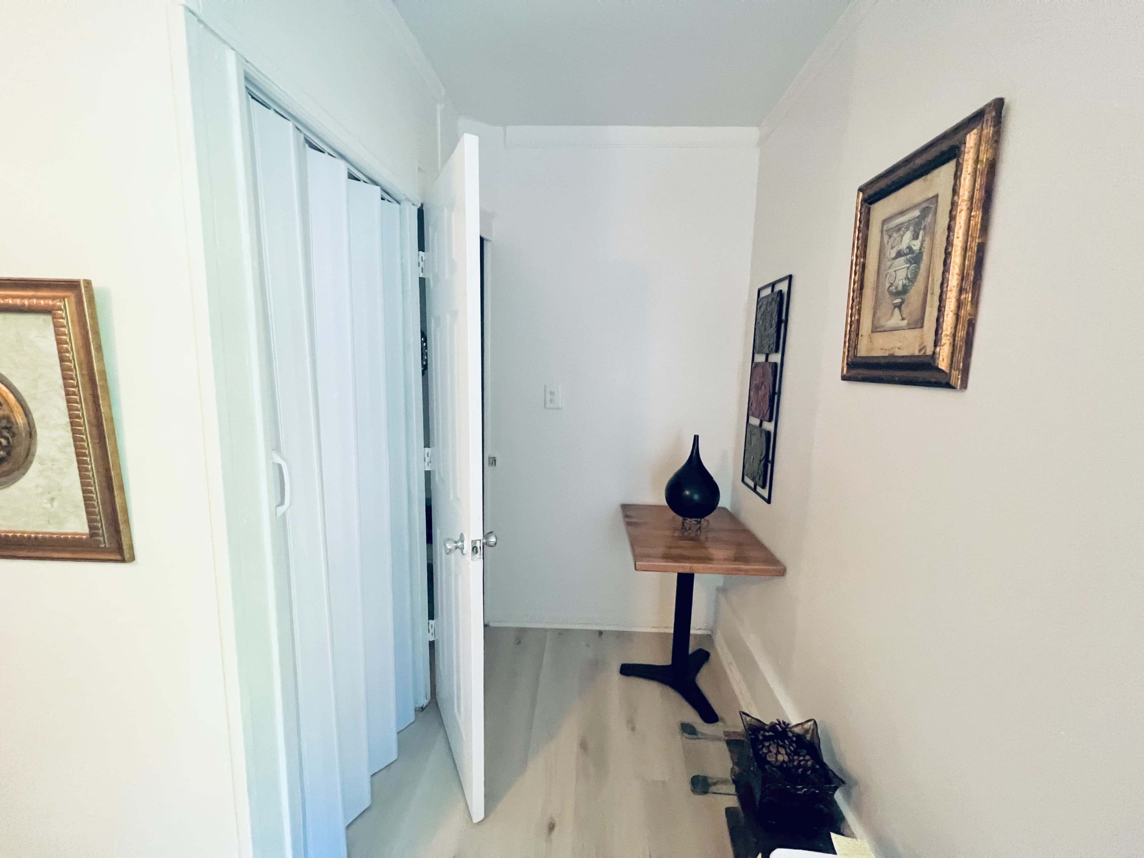 A corner of a room featuring an open door, a wooden table against the wall, and decorative wall art.