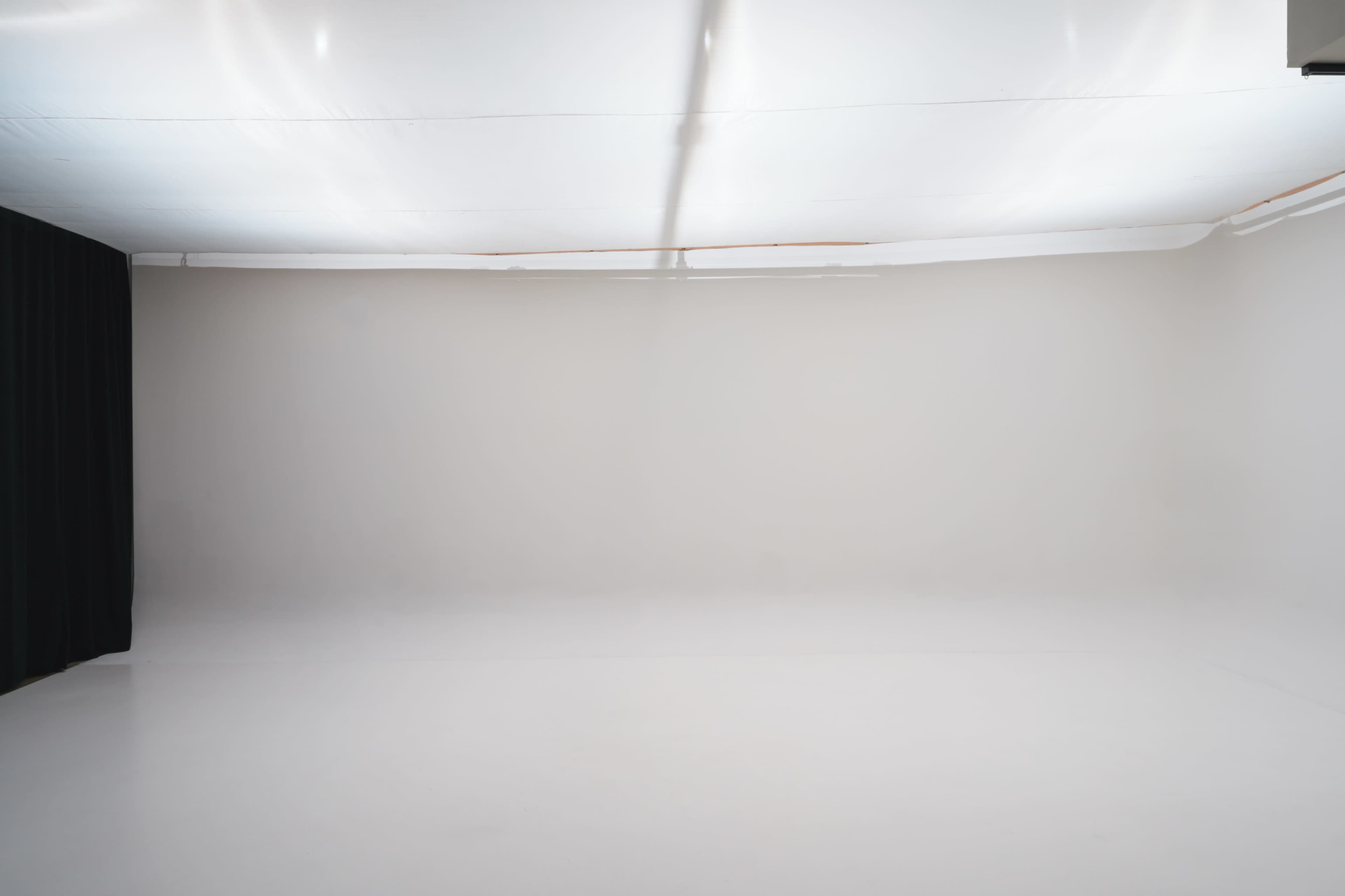 The image shows a spacious, empty studio with a white floor and walls, and a black curtain on one side.