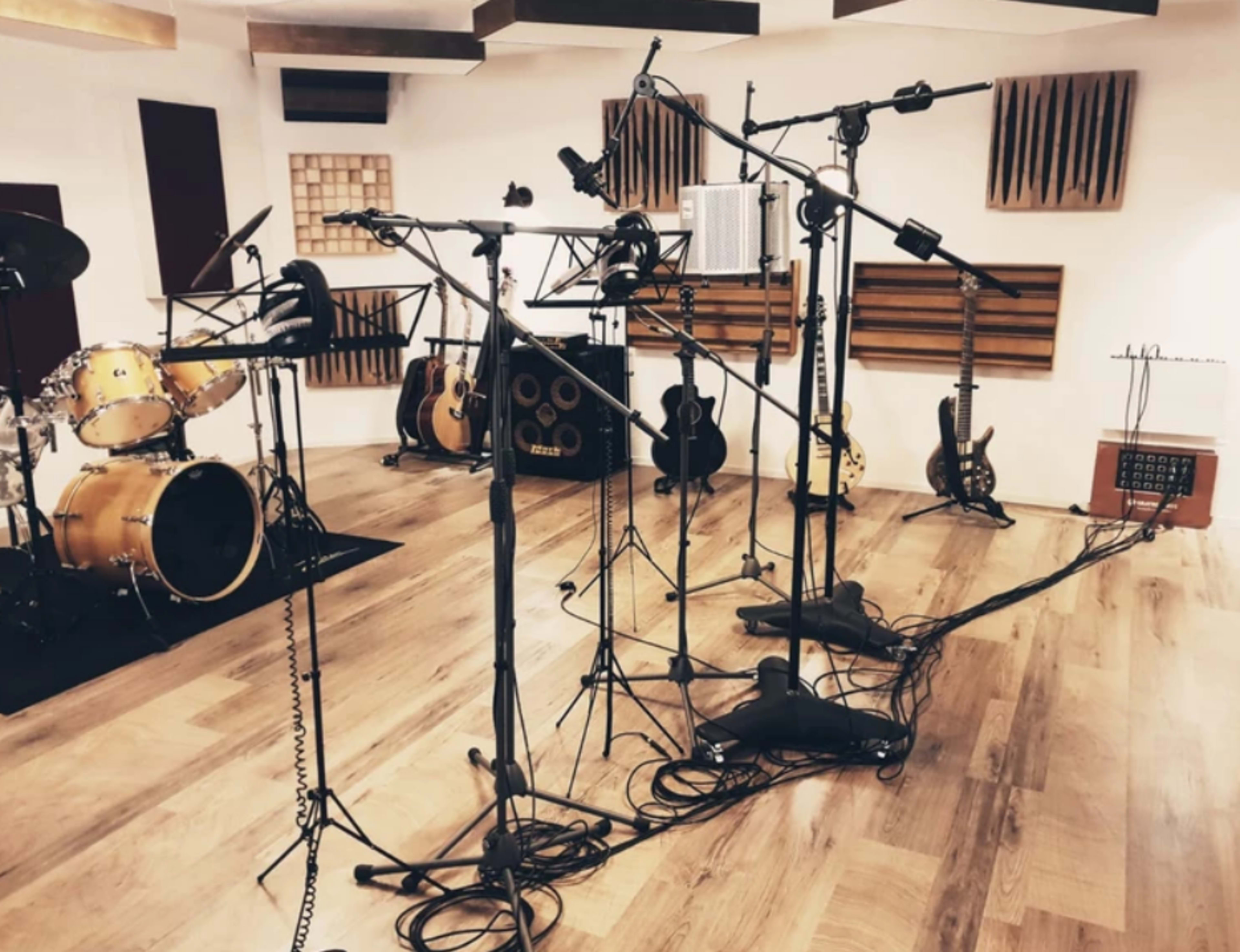 The image shows a recording studio with microphones setup around a drum kit and various musical instruments in the background.