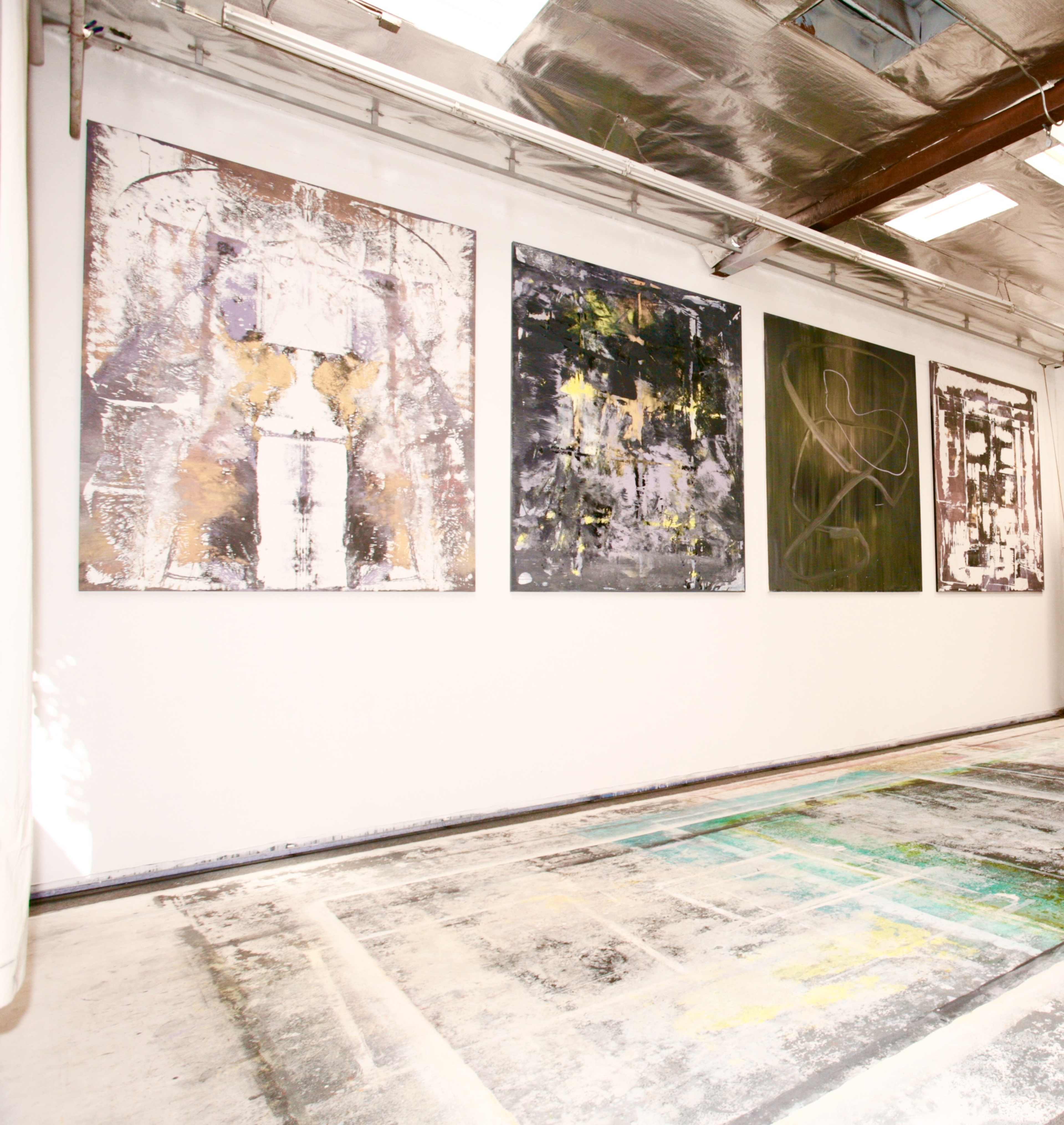 The image shows a gallery space with four large abstract paintings displayed on a white wall, alongside a patterned floor.