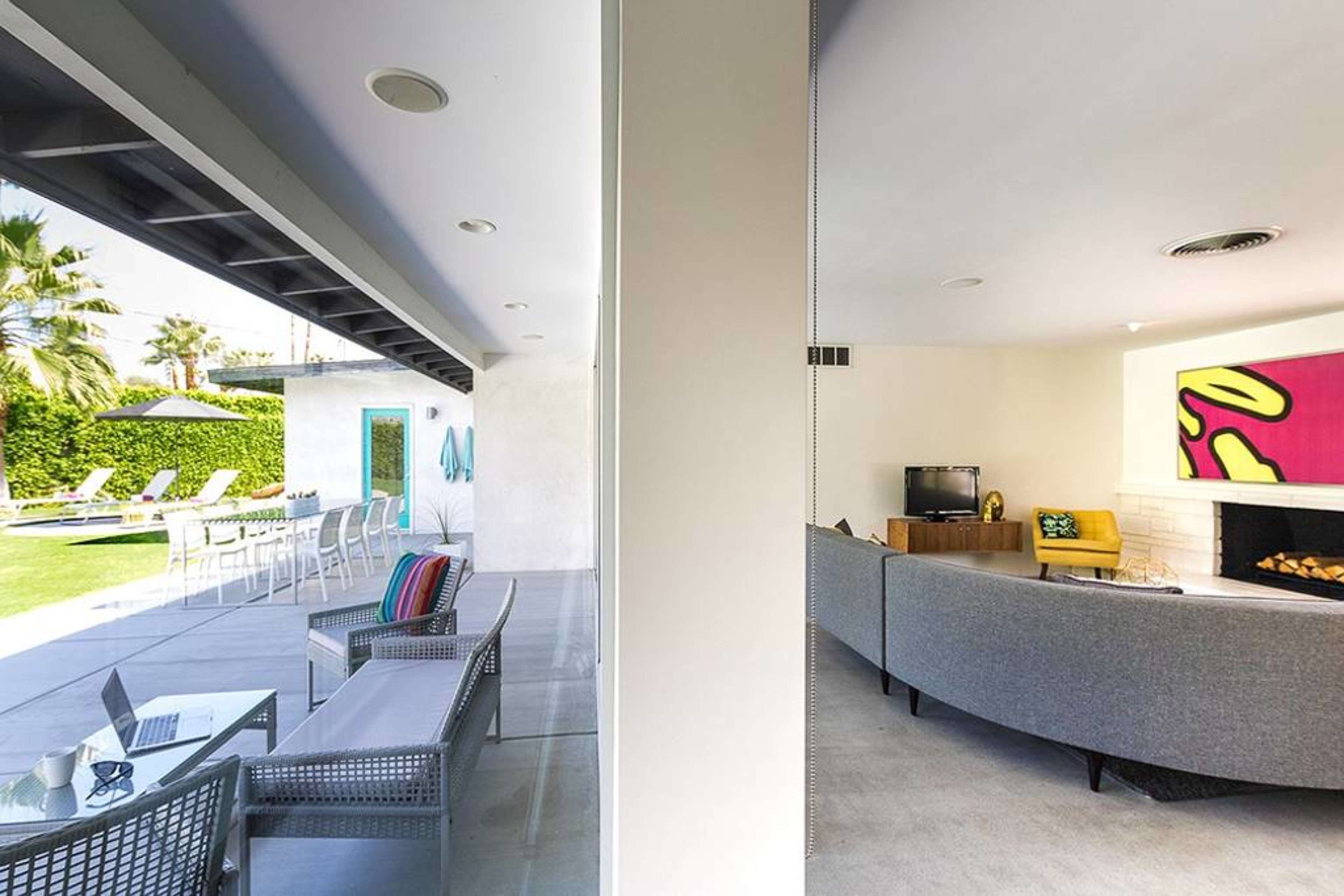 A split scene of a modern indoor living area with a gray sofa and a TV, adjacent to an outdoor space featuring a pool and lounge chairs.