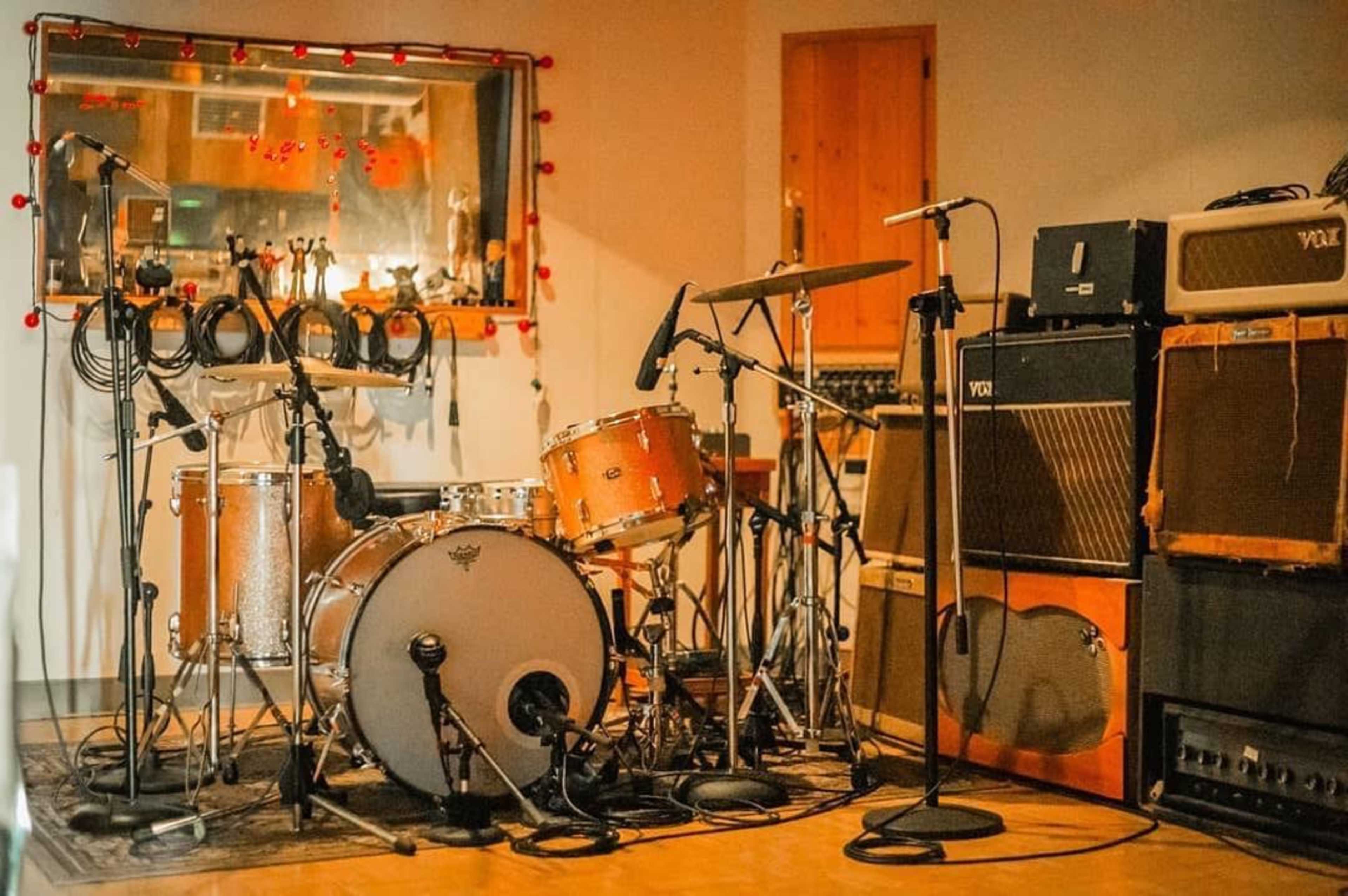 A recording studio with a vintage drum set positioned in front of amplifiers and microphones.