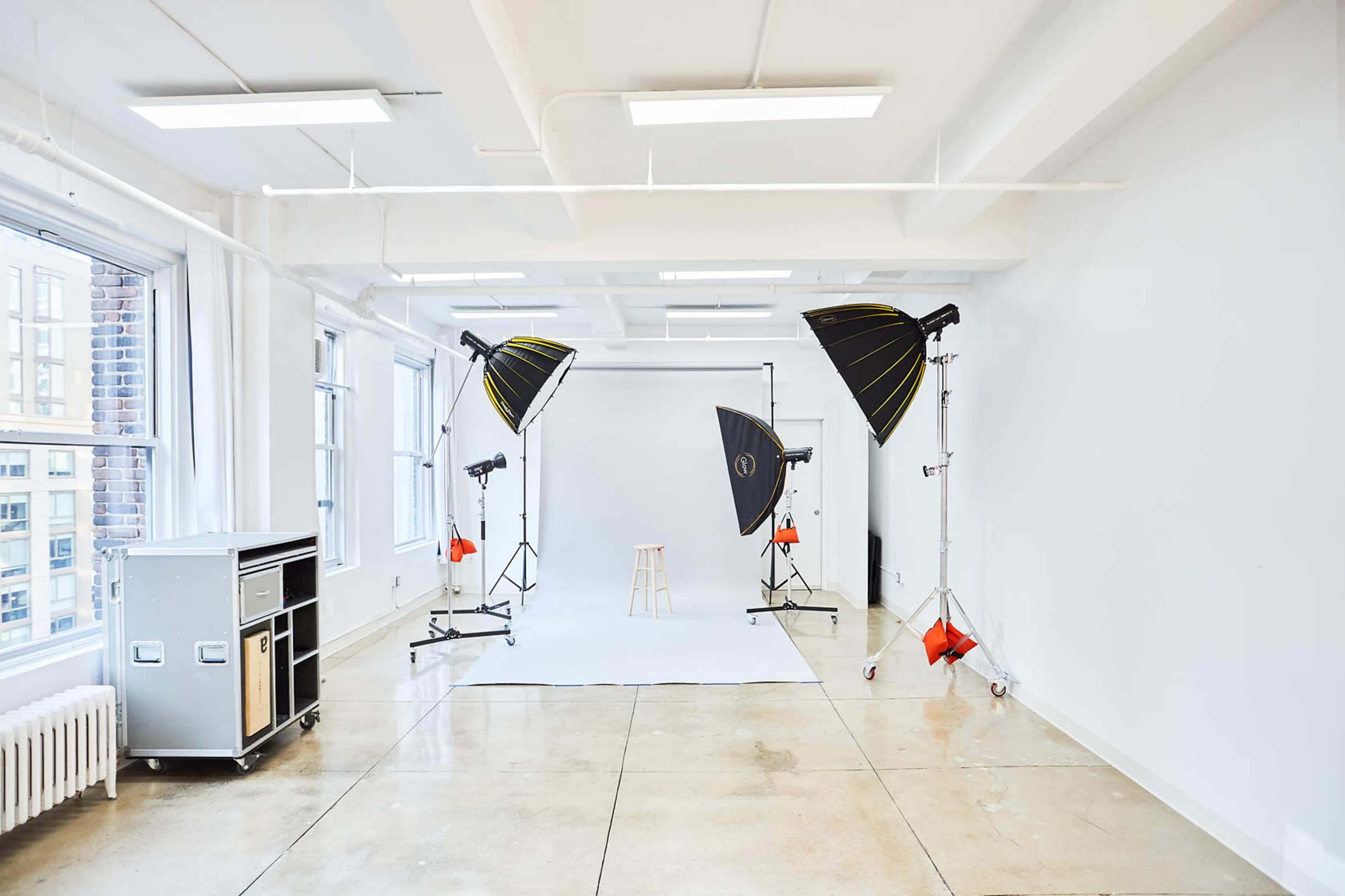 The image shows a well-lit photography studio featuring a backdrop, a stool, and multiple lighting setups.