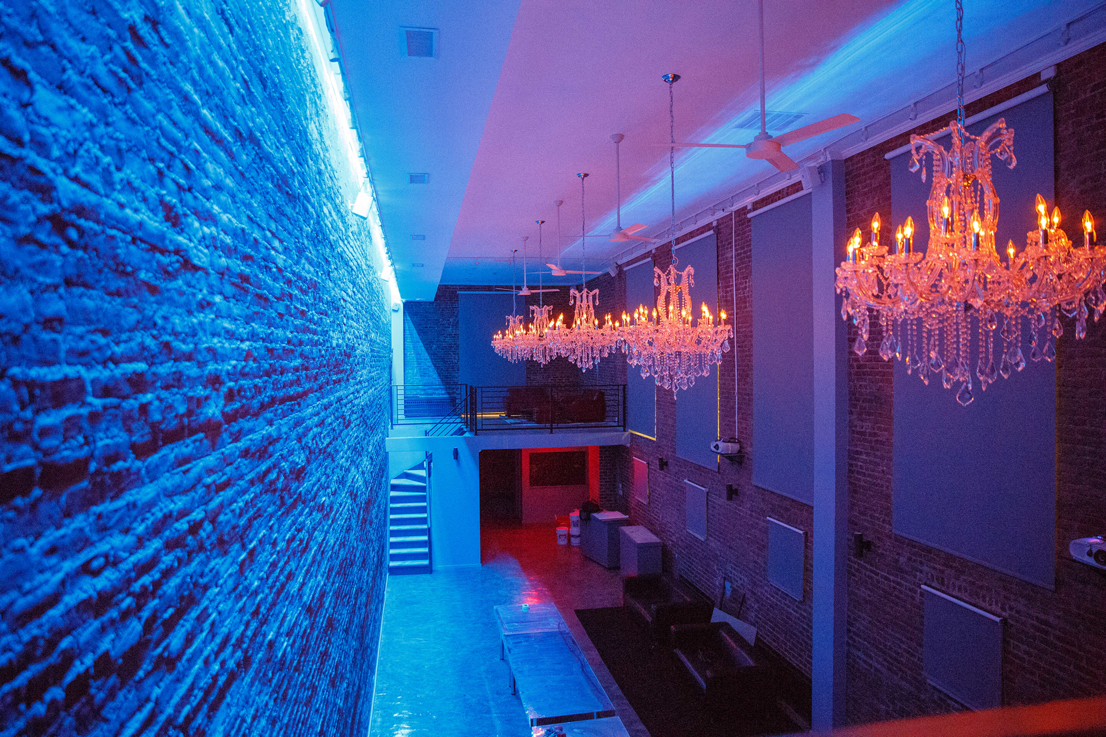 The scene shows a modern interior space with exposed brick walls, colorful lighting, and elegant chandeliers hanging from the ceiling.