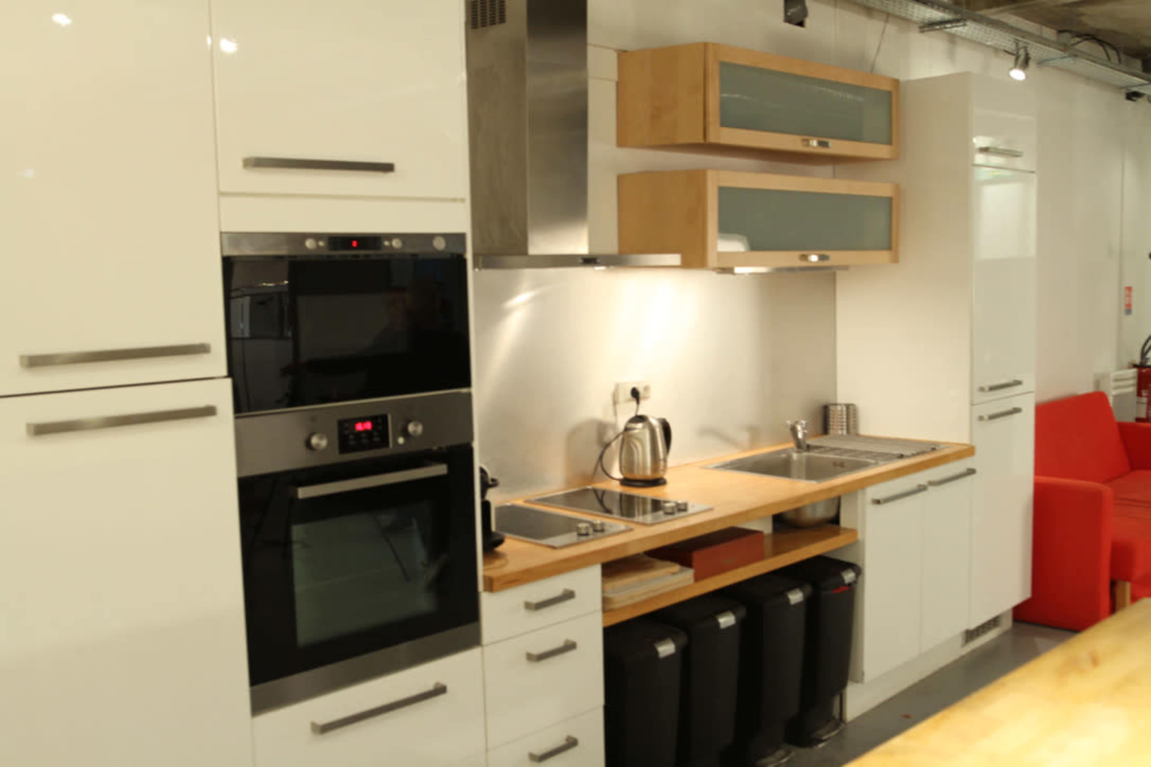 A modern kitchen with white cabinetry, stainless steel appliances, and a wooden countertop alongside a sink and garbage bins.
