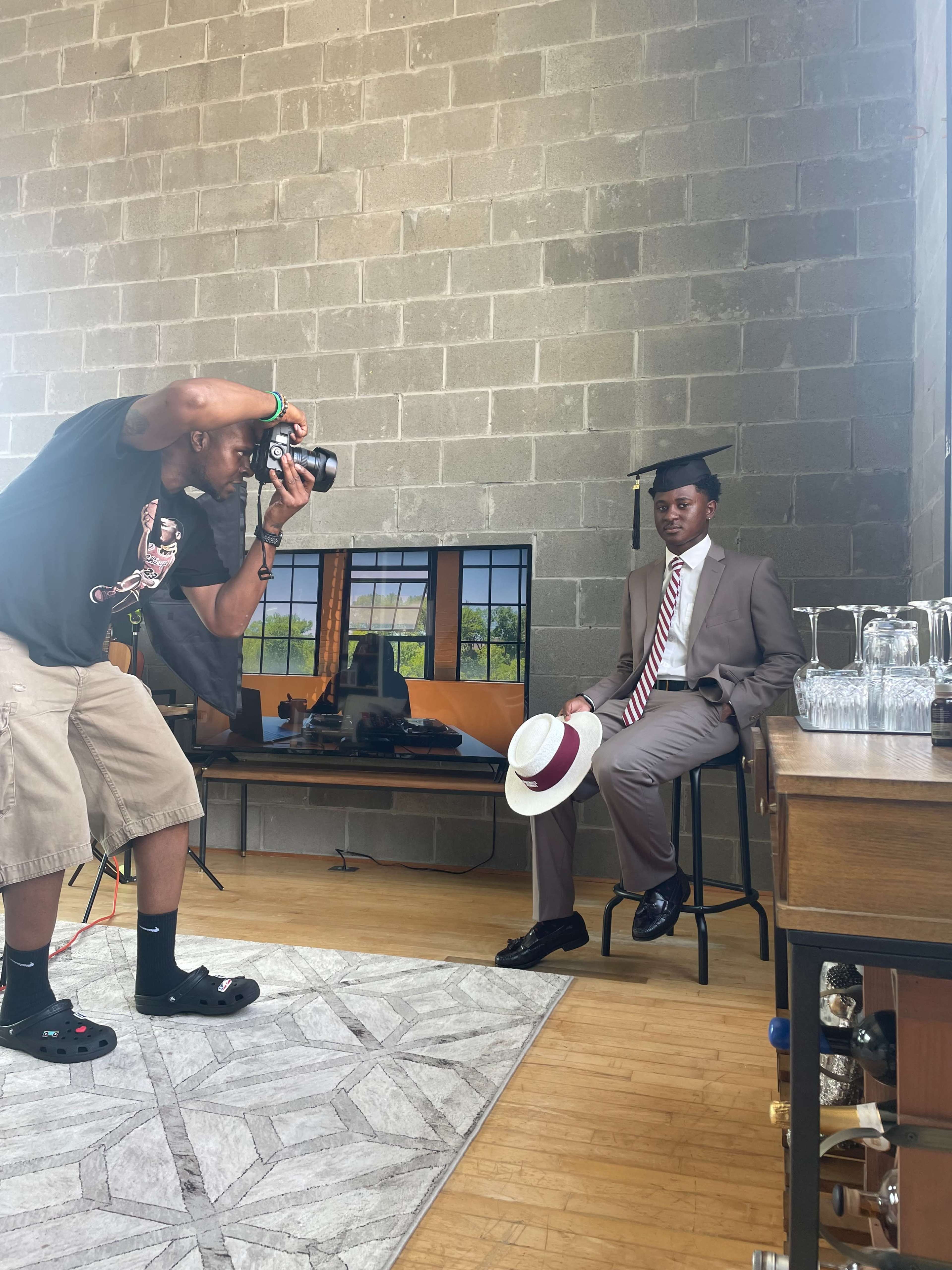 A photographer captures a graduate wearing a cap and gown while seated in a stylish interior.